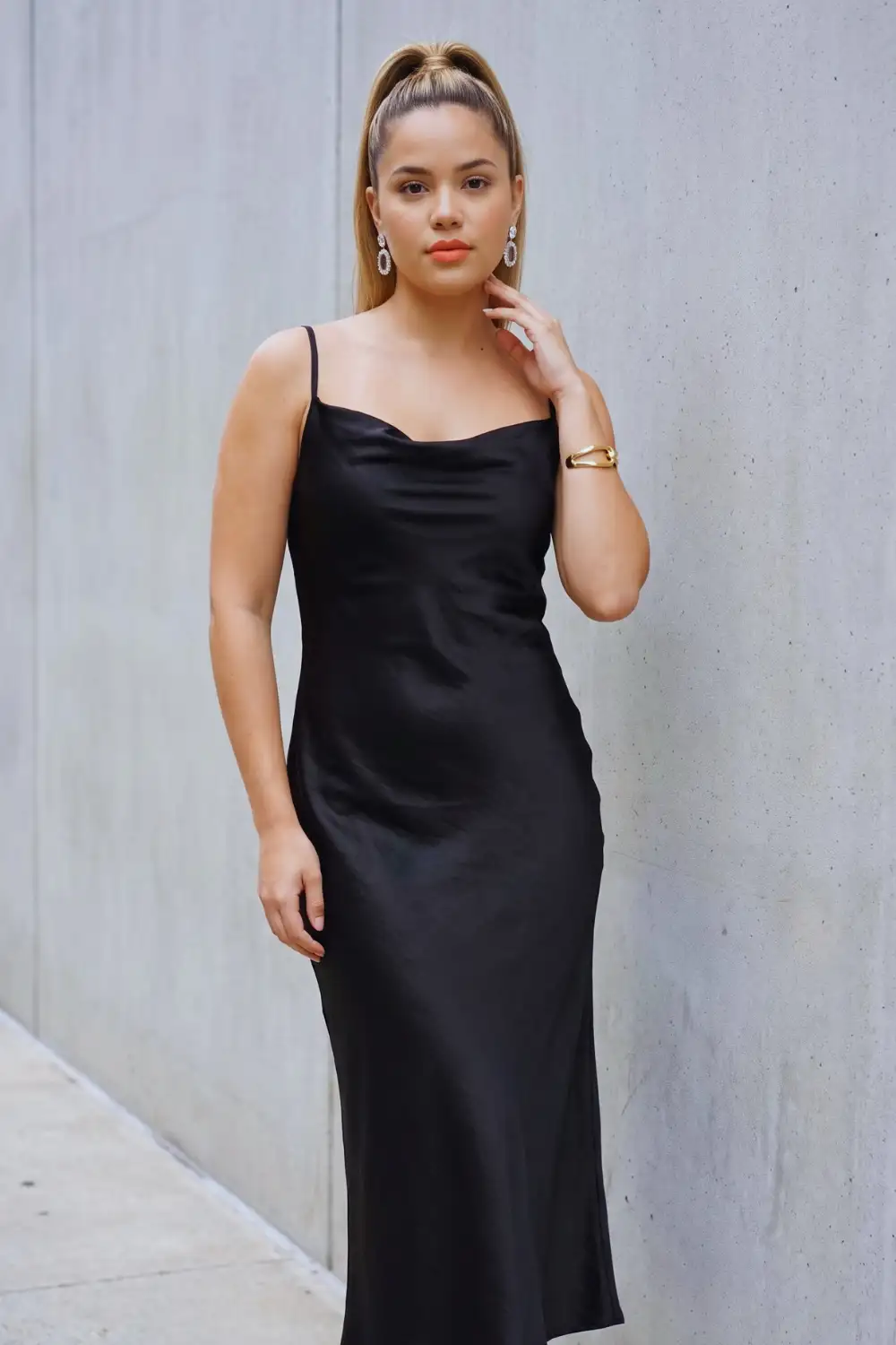 Woman in black satin cowl neck fitted slip midi dress with thin straps