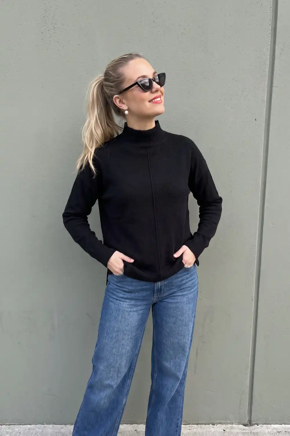 Woman in black seam detail turtleneck knit sweater with blue wide leg jeans