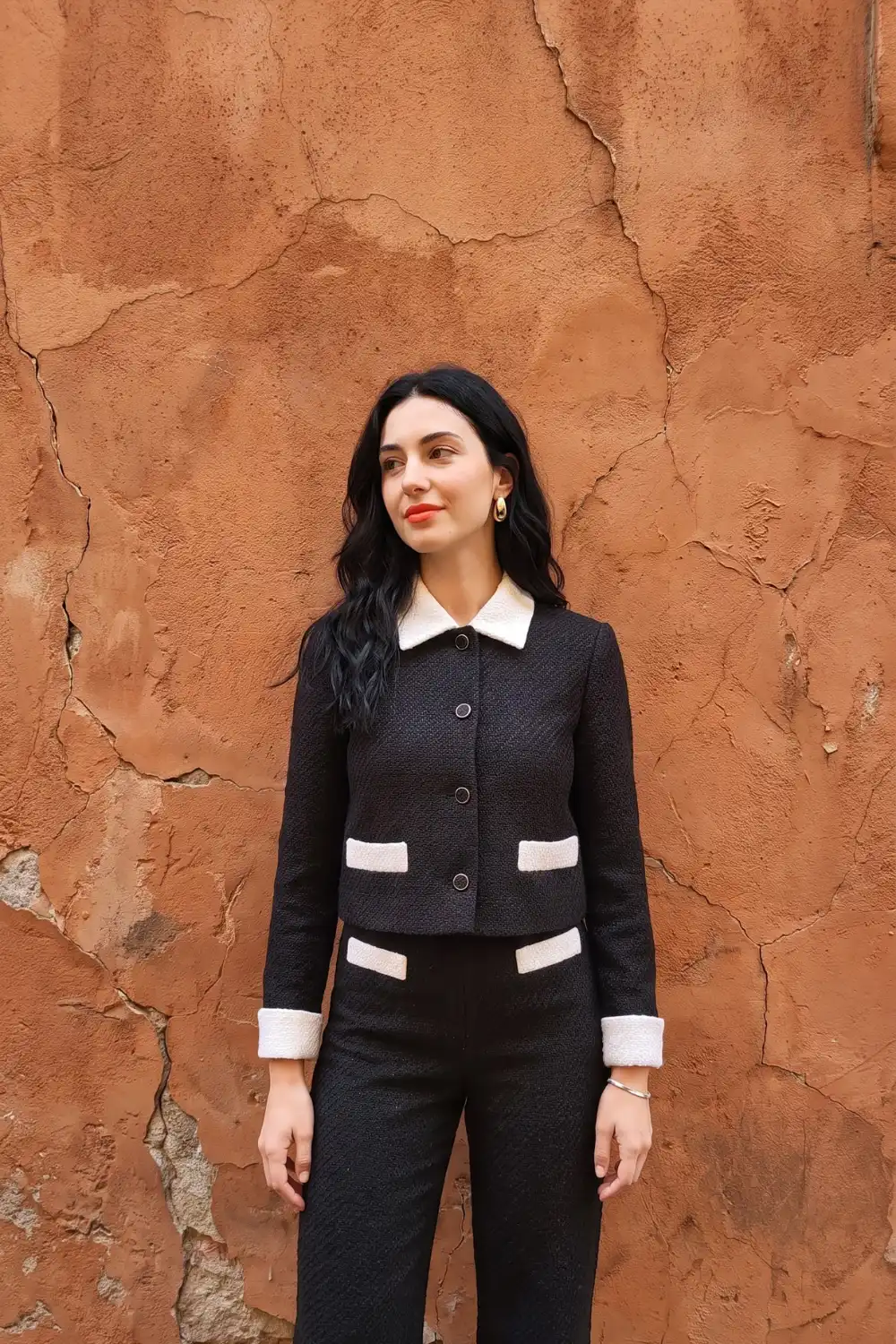 Woman in black tweed cropped jacket with cream contrast trim and black straight trousers