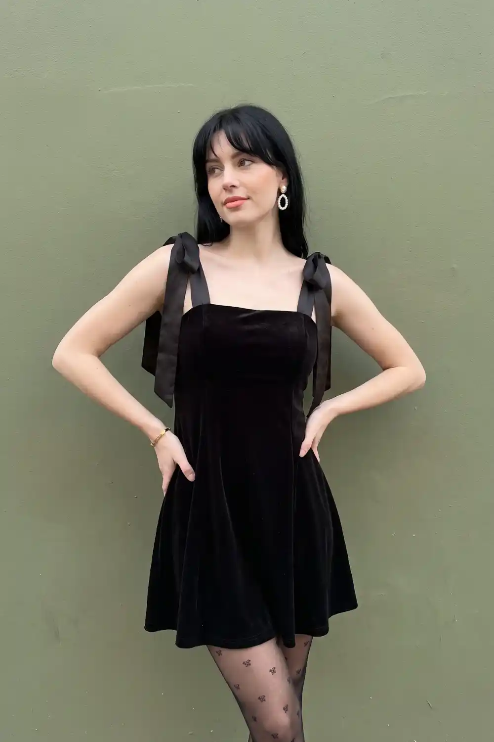 Woman in black velvet bow strap square neck mini dress with floral tights