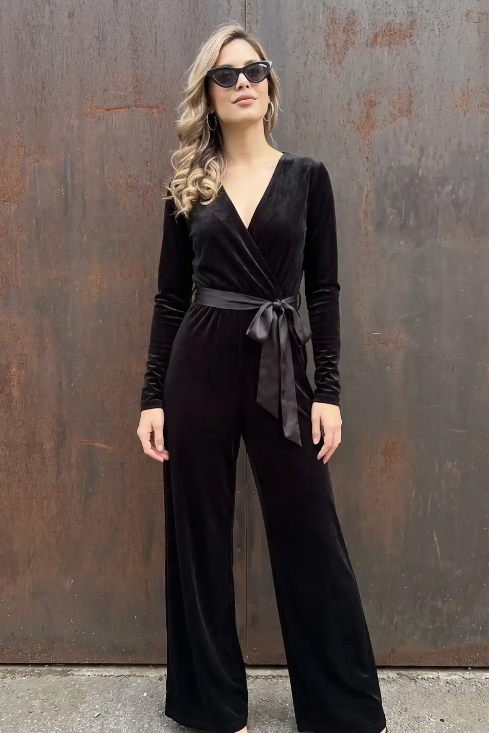 Woman in black velvet long sleeve wrap wide leg jumpsuit with satin tie waist