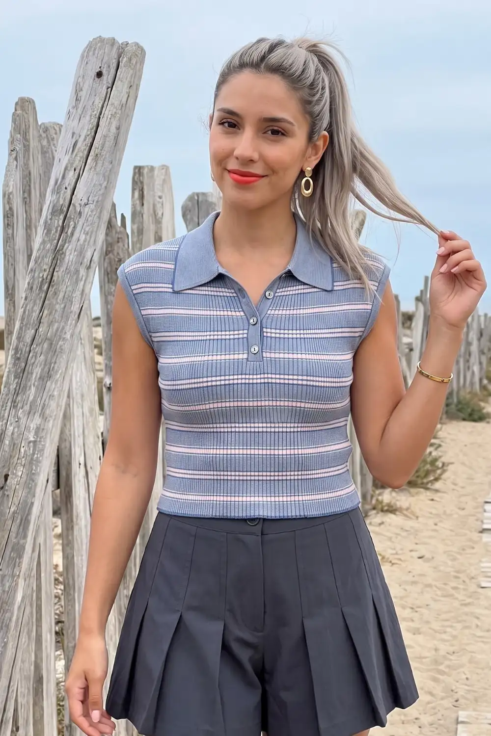 Woman in blue pink stripe sleeveless knit polo top with dark grey pleated shorts