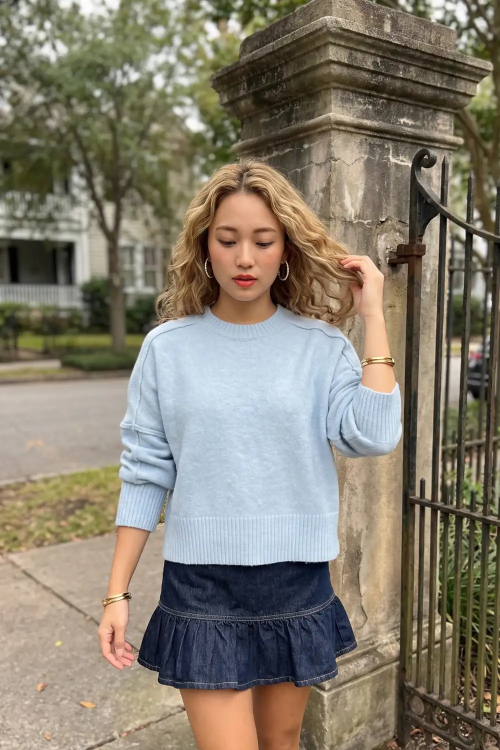 Woman in baby blue oversized crew neck sweater with dark navy denim ruffle hem mini skirt