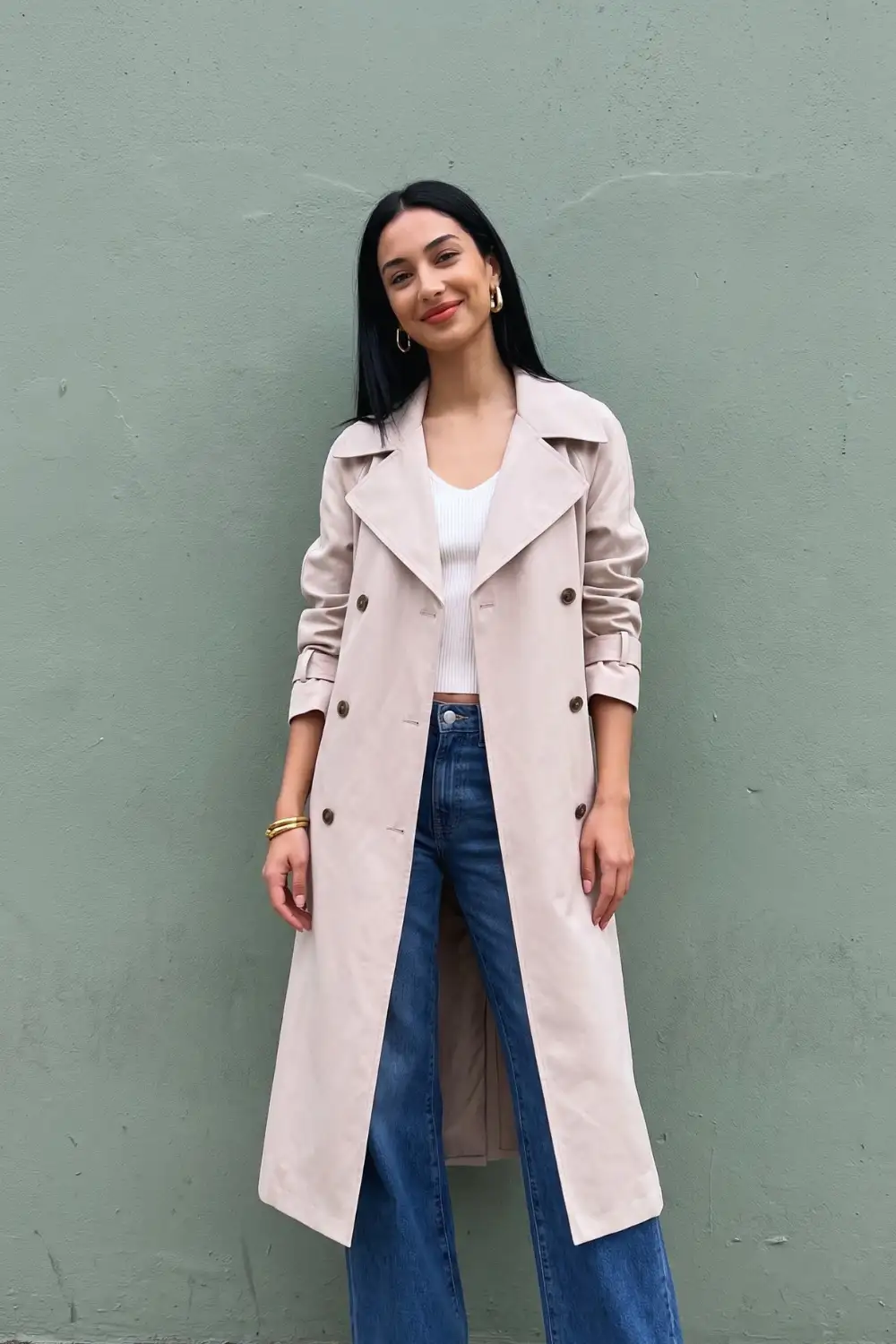 Woman in light blush pink maxi trench coat with white ribbed crop top and dark wide leg jeans