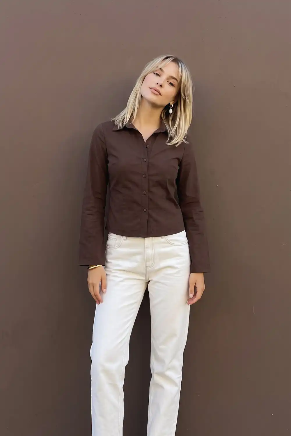 Woman in dark chocolate brown fitted button-up shirt with cream white straight leg jeans