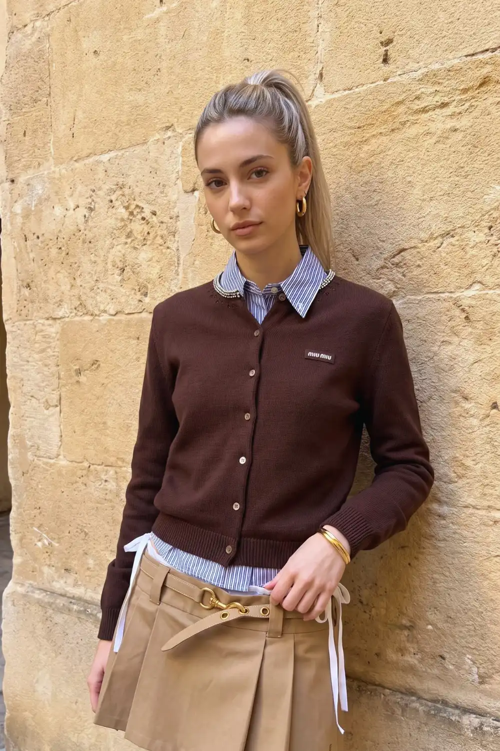 Woman in dark brown knit cardigan layered over blue stripe shirt with beige wide leg trousers