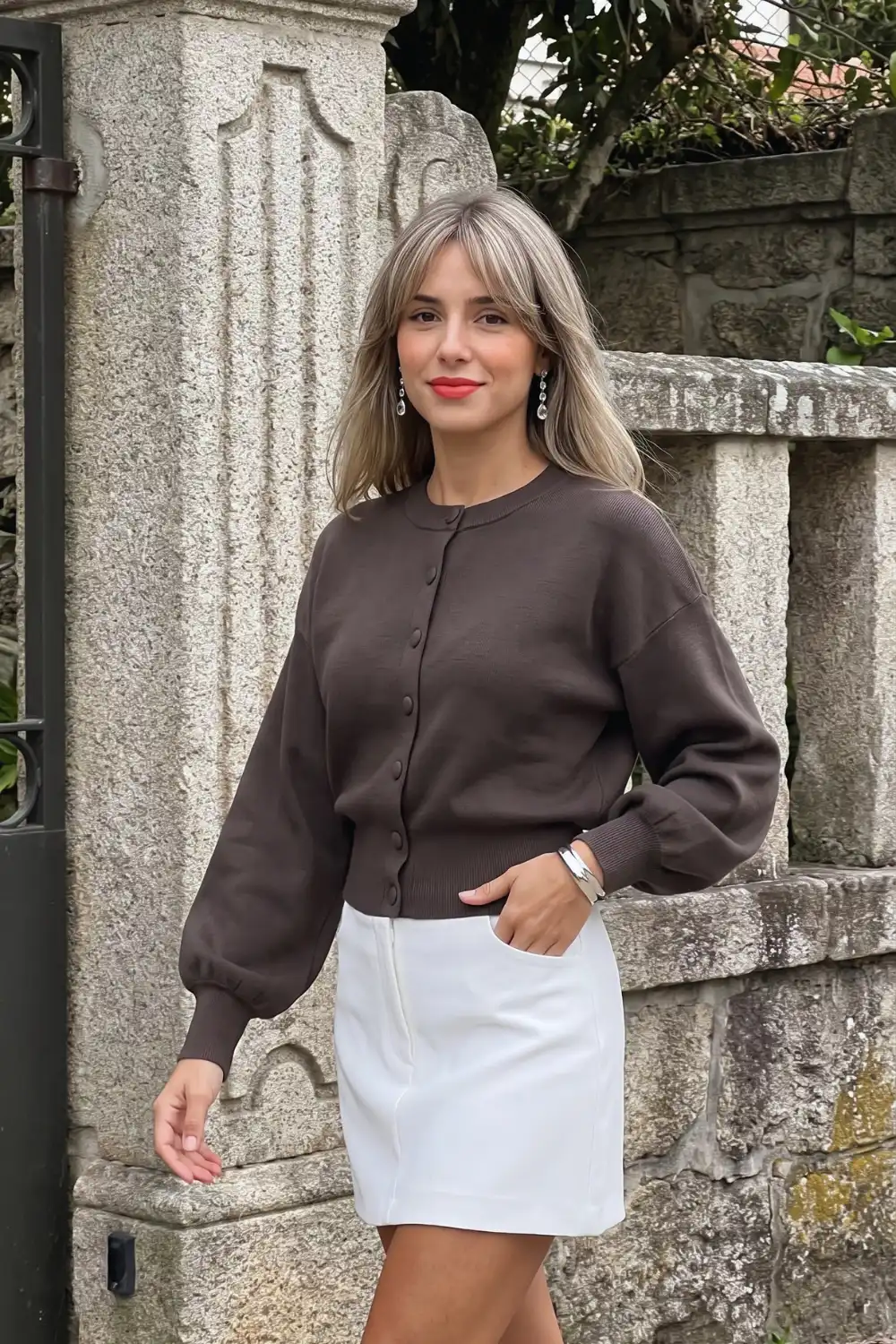 Woman in chocolate brown balloon sleeve crew neck cardigan with white mini skirt