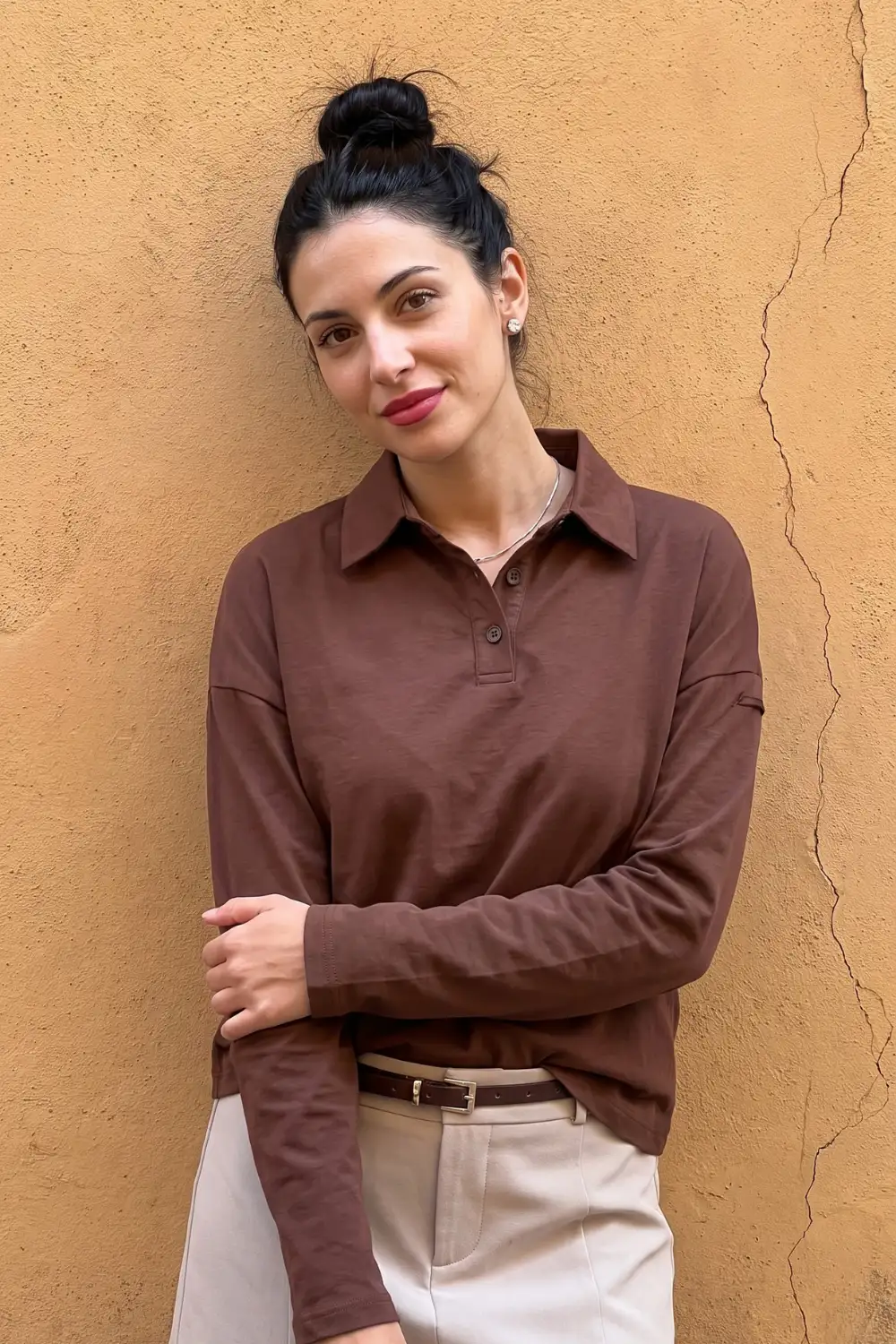 Woman in chocolate brown long sleeve polo shirt with cream belted trousers