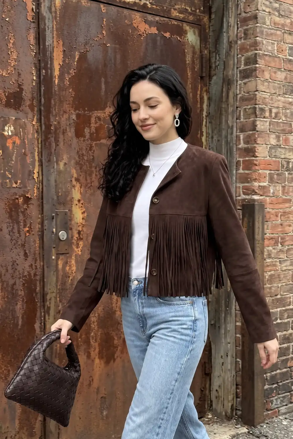 Woman in brown suede fringe cropped jacket with white turtleneck and light wash wide leg jeans