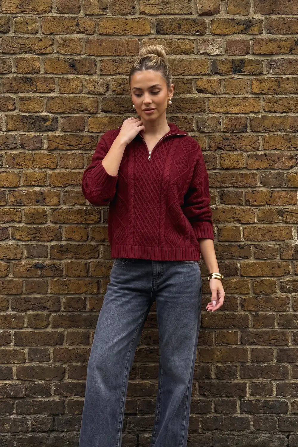 Woman in burgundy cable knit half zip oversized sweater with dark grey wide leg jeans