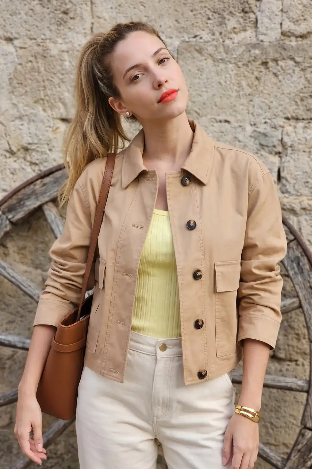 Woman in camel button-up shirt jacket with yellow ribbed tank and cream wide leg jeans