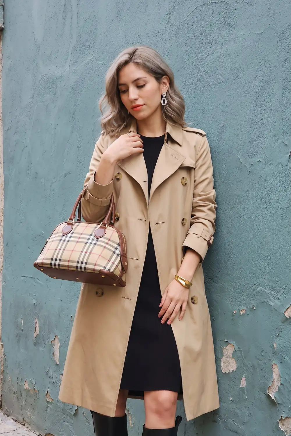 Woman in camel double-breasted trench coat with black mini dress and knee high boots