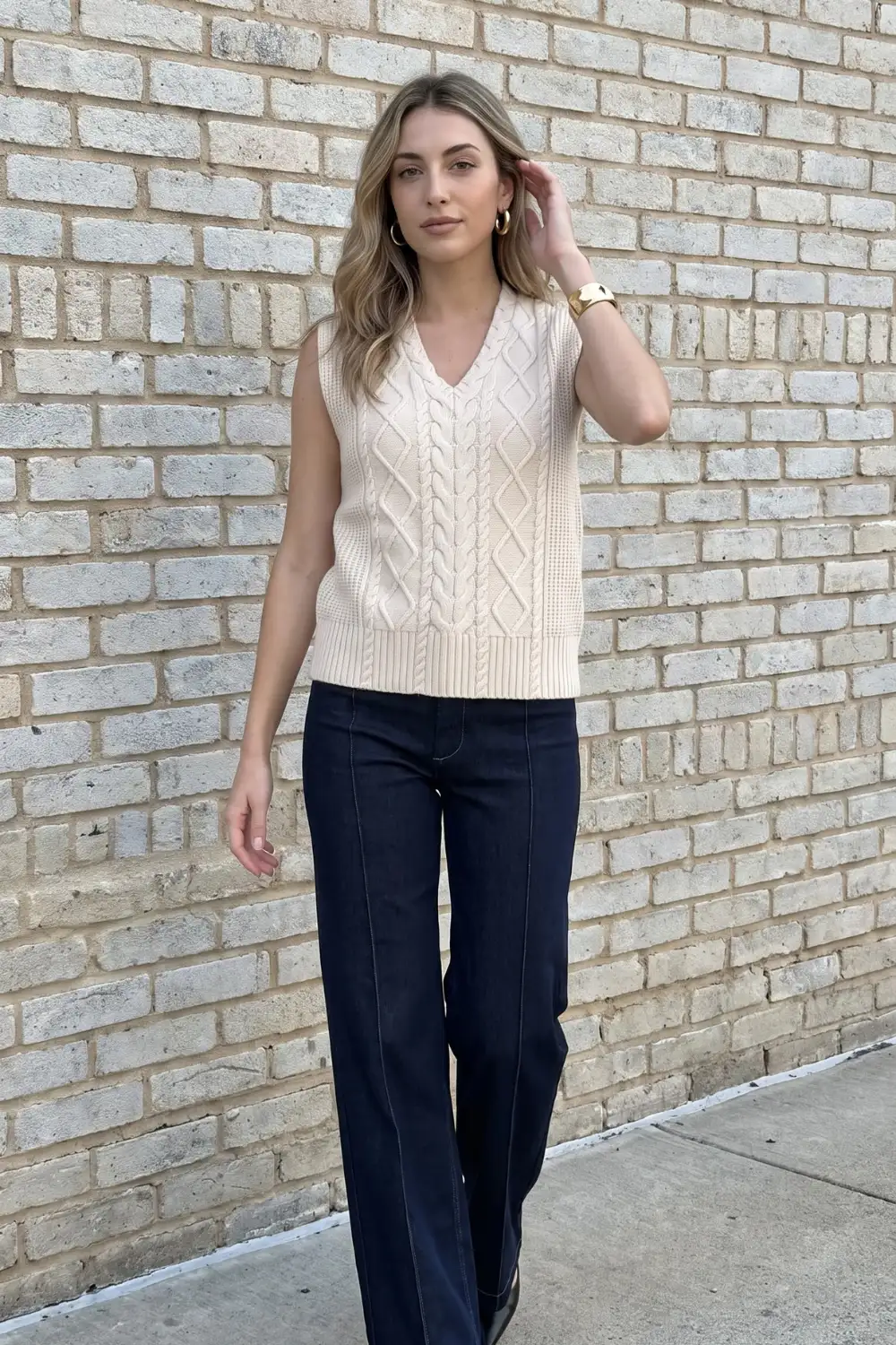 Woman in cream cable knit v neck sweater vest with dark navy wide leg jeans