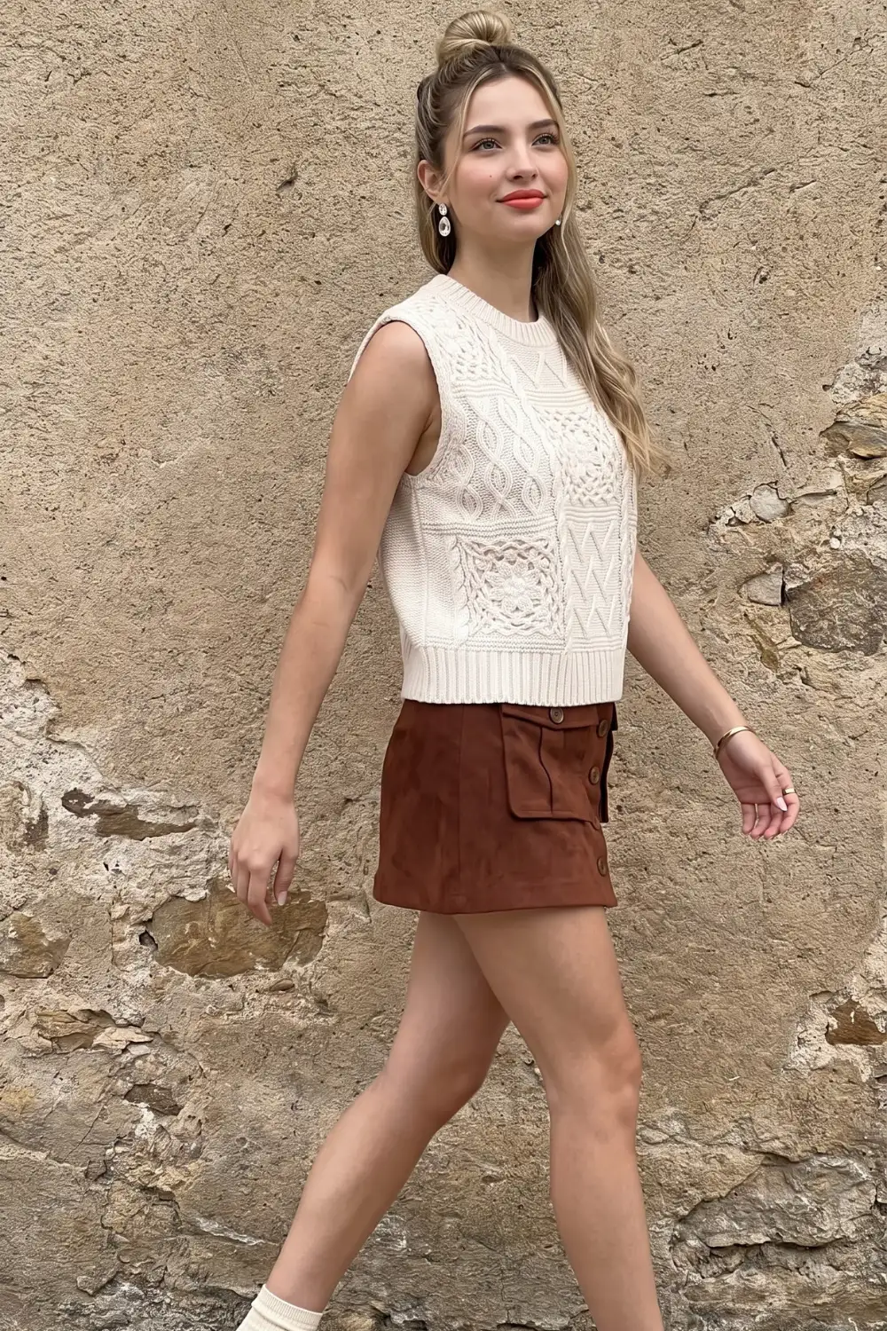Woman in cream mixed cable knit sweater vest with rust brown suede button mini skirt