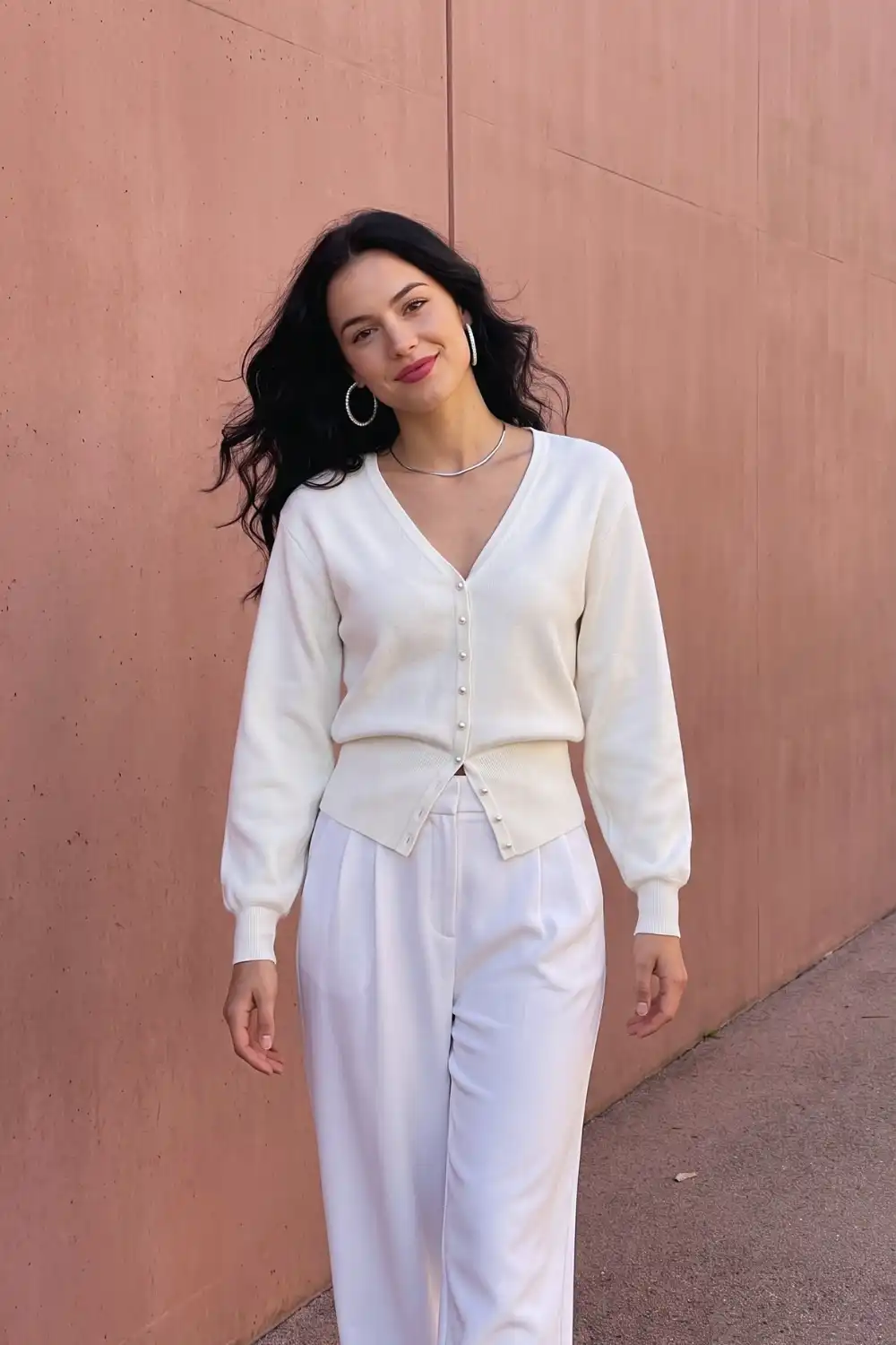 Woman in cream pearl button v neck knit cardigan with white wide leg tailored trousers