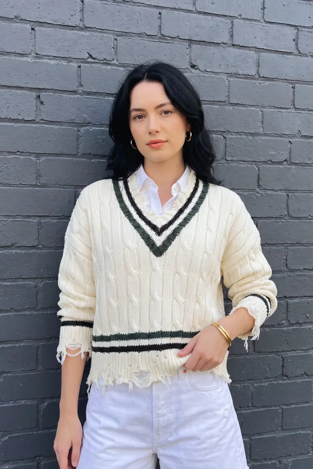 Woman in cream cable knit cricket v neck sweater over white shirt with white jeans