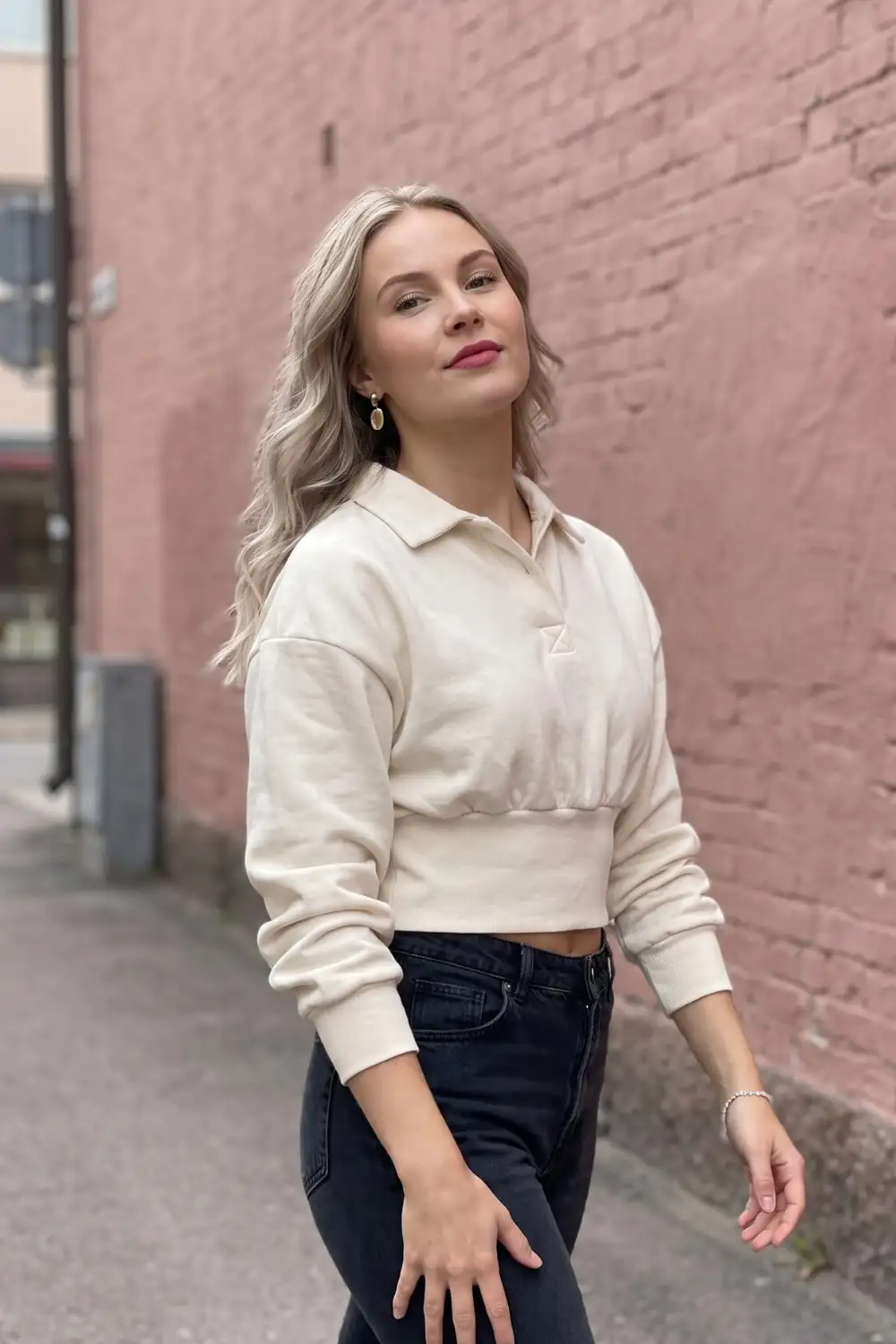 Woman in cream oversized cropped polo sweatshirt with dark navy jeans