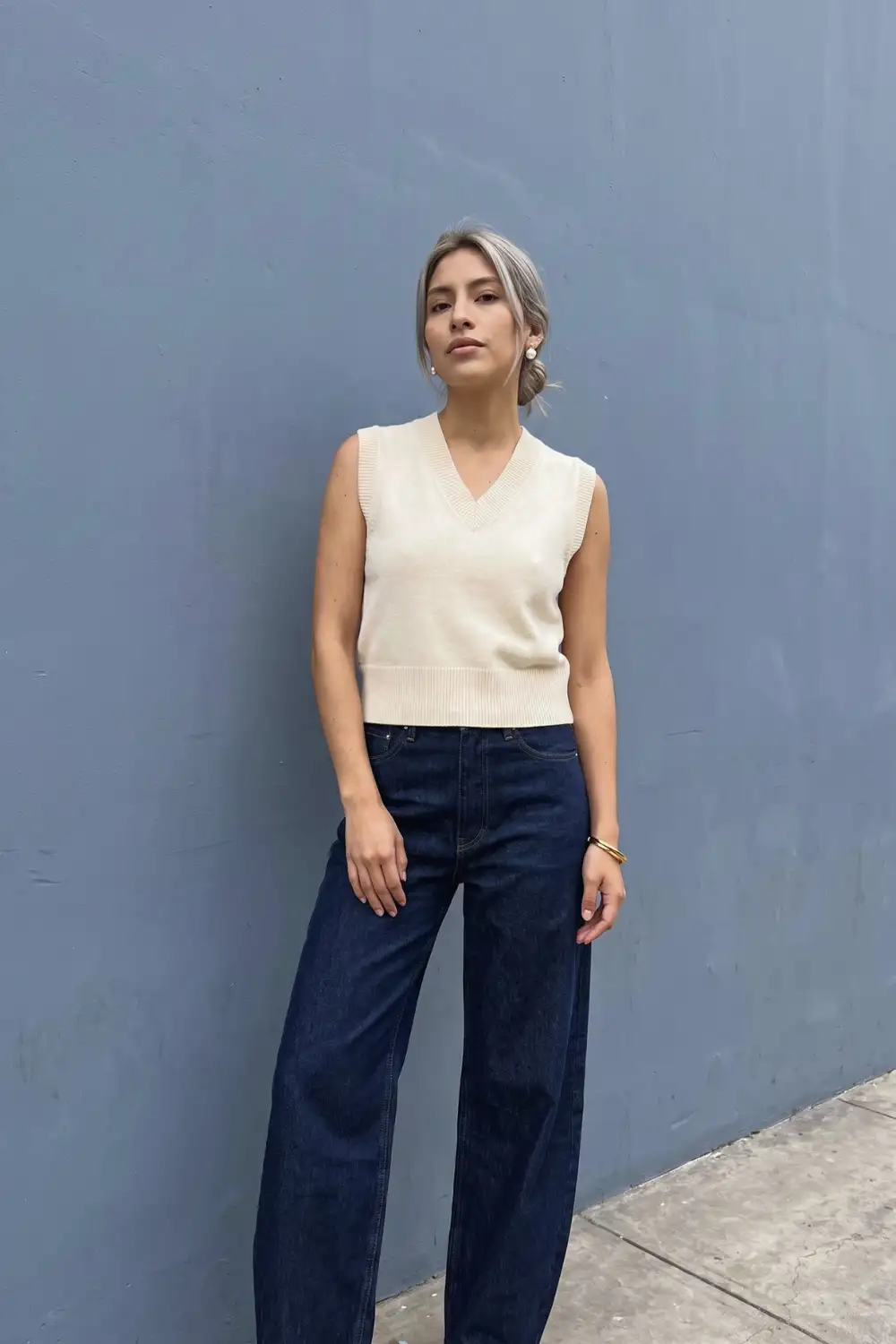 Woman in cream plain v neck knit sweater vest with dark navy wide leg jeans