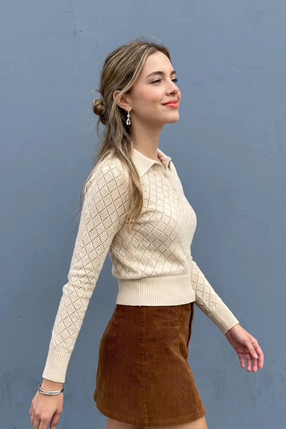 Woman in cream diamond pointelle knit polo top with brown corduroy mini skirt
