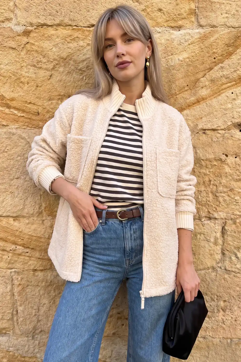 Woman wearing cream teddy fleece zip jacket with stripe top and light wash jeans