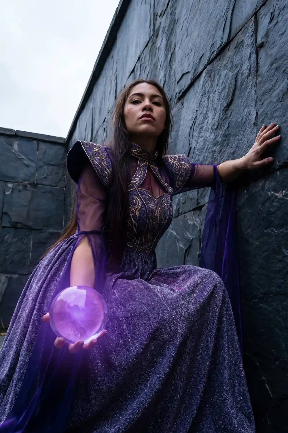 Woman dressed as dark sorceress in purple glitter gown holding glowing crystal ball