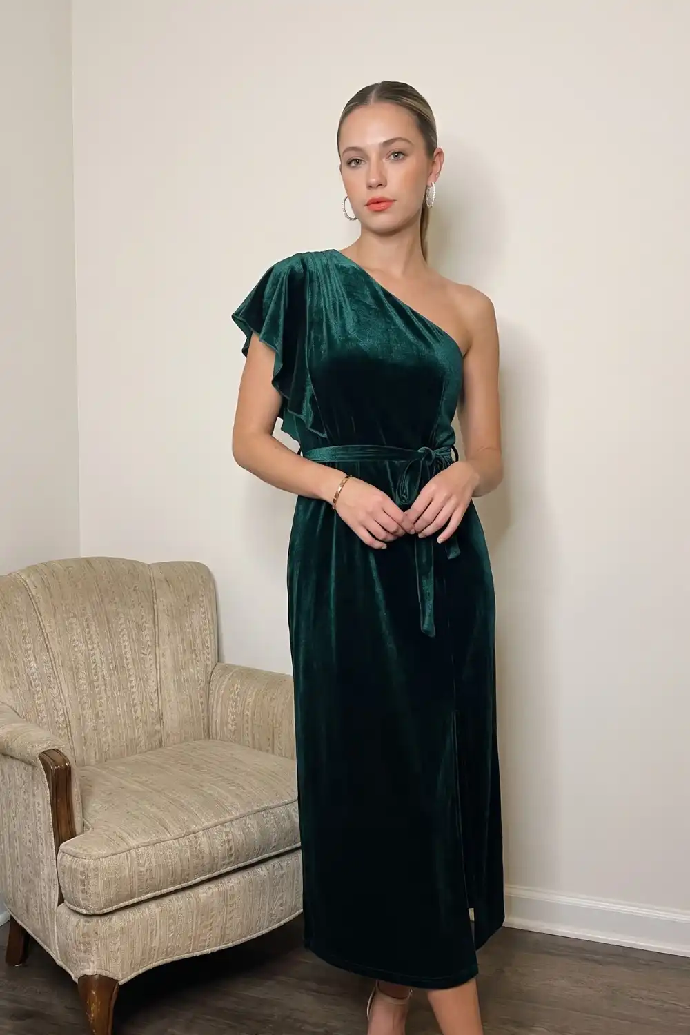 Woman in emerald green velvet one shoulder ruffle belted midi dress
