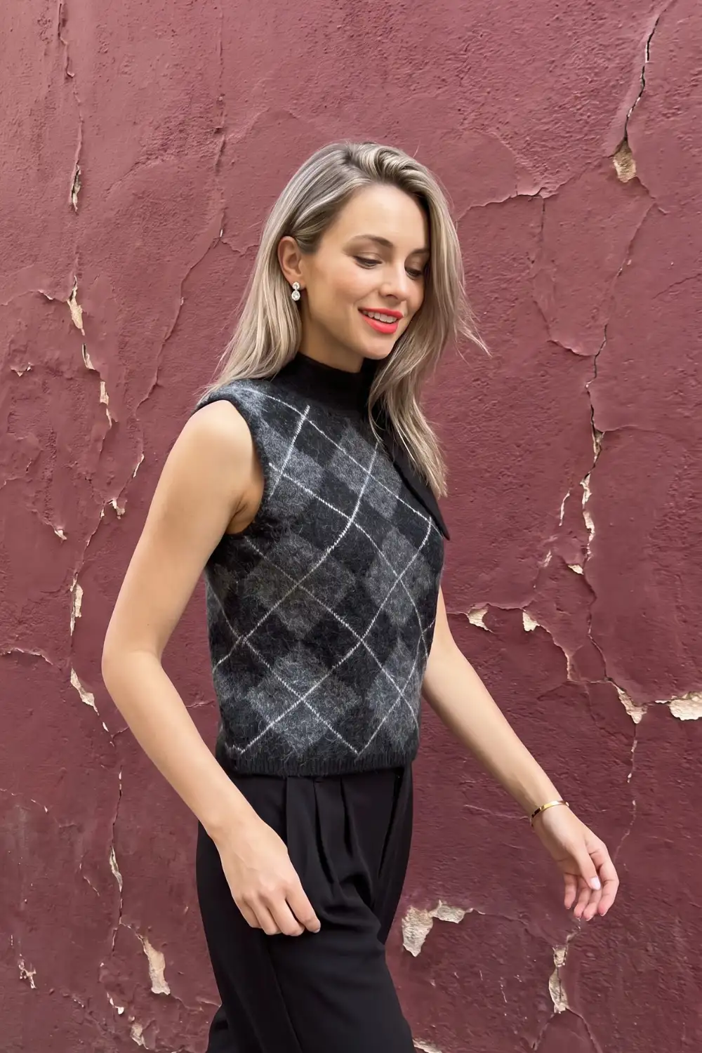 Woman in charcoal grey argyle fuzzy knit vest over black turtleneck with black trousers