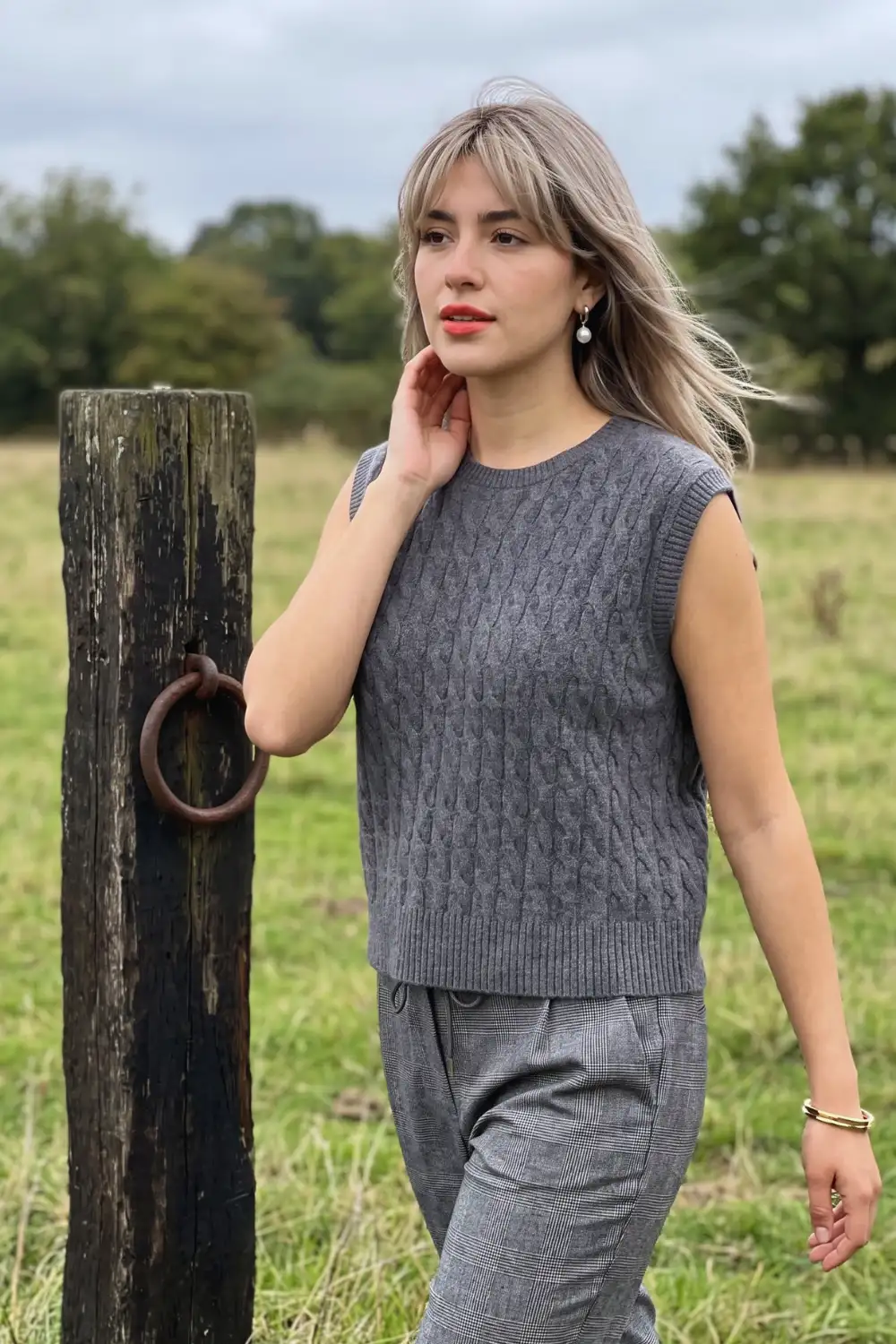 Woman in charcoal grey cable knit crew neck sweater vest with grey plaid wide leg trousers