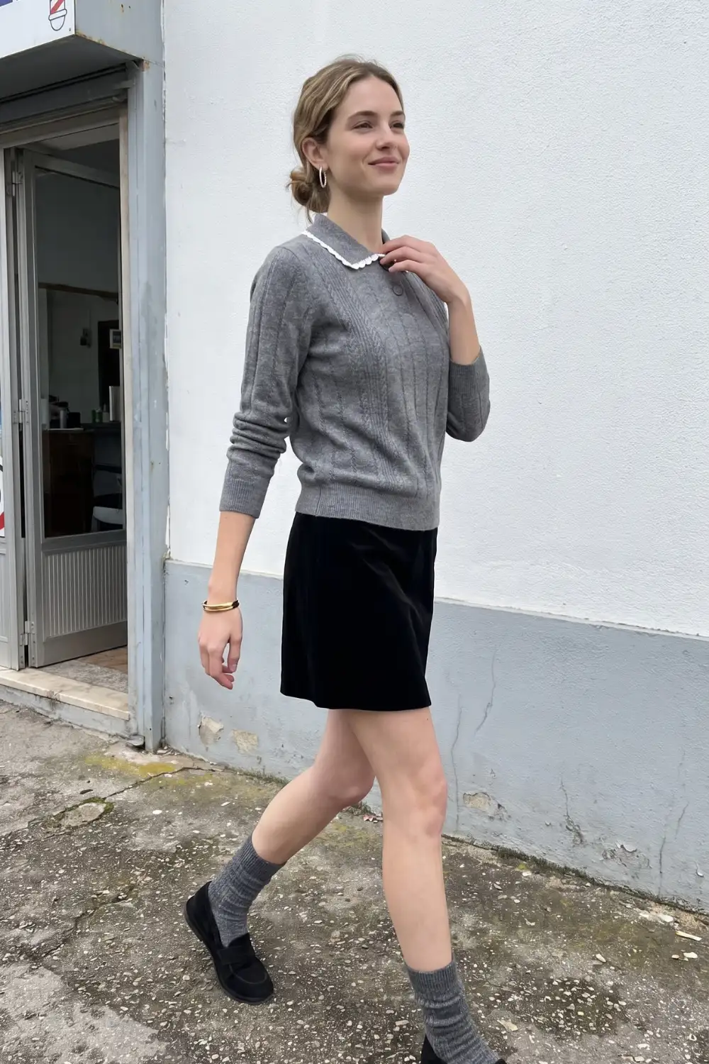Woman in grey cable knit peter pan collar sweater with black velvet mini skirt and loafers
