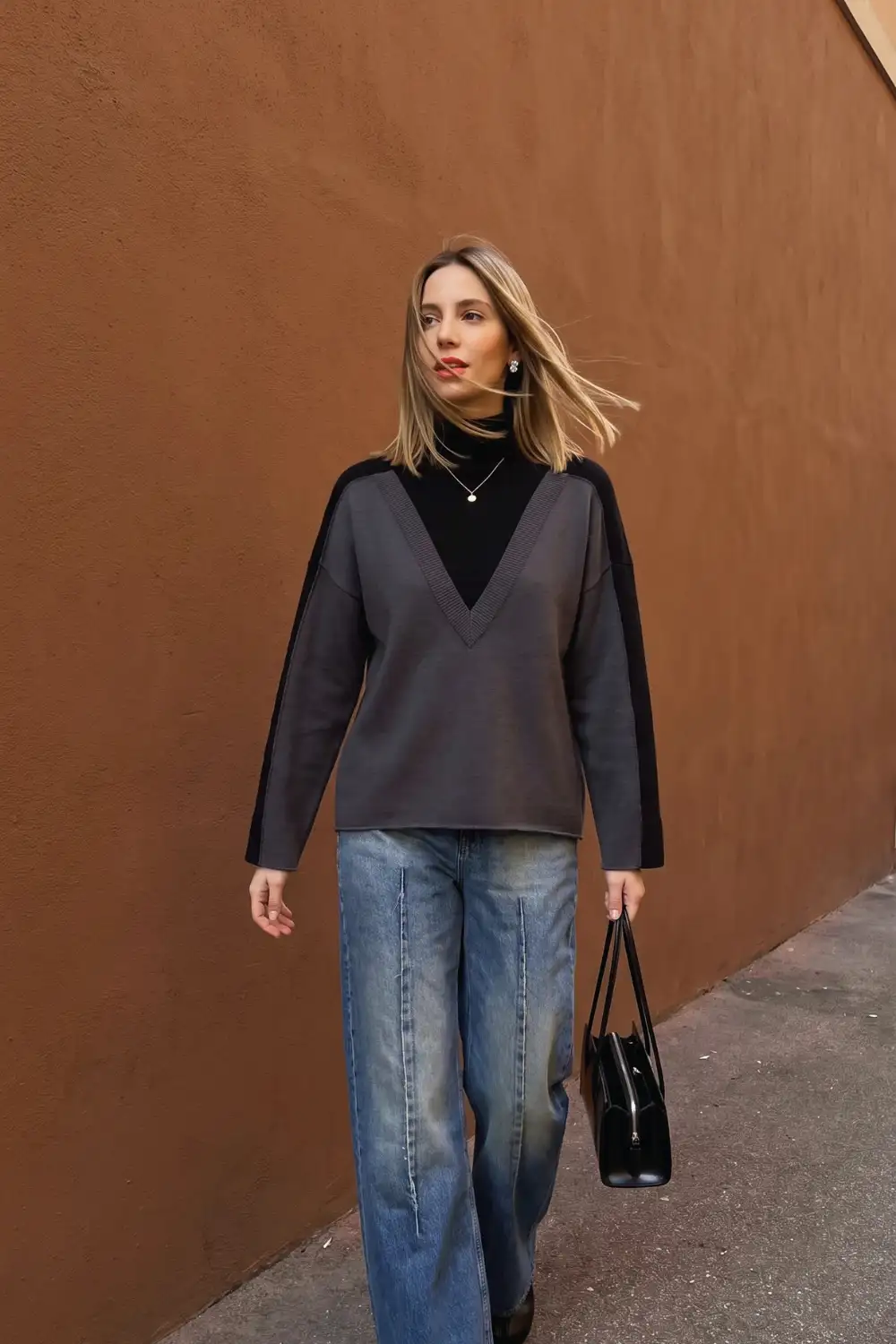 Woman in charcoal grey v neck oversized sweater over black turtleneck with wide leg jeans