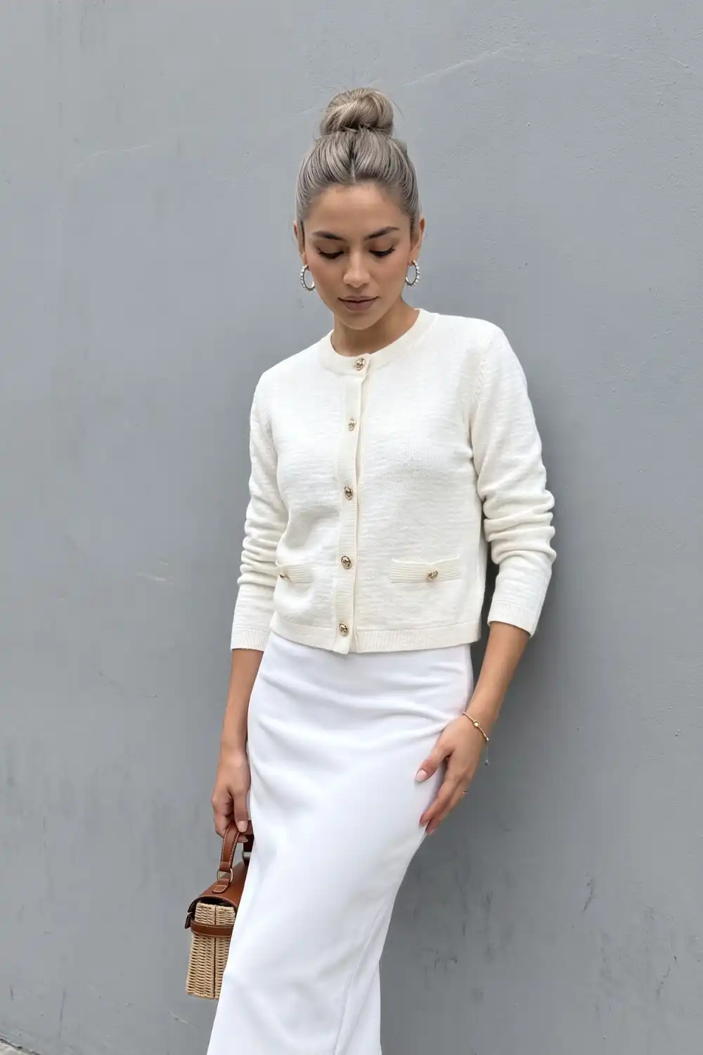 Woman in ivory cropped gold button cardigan with white satin maxi skirt