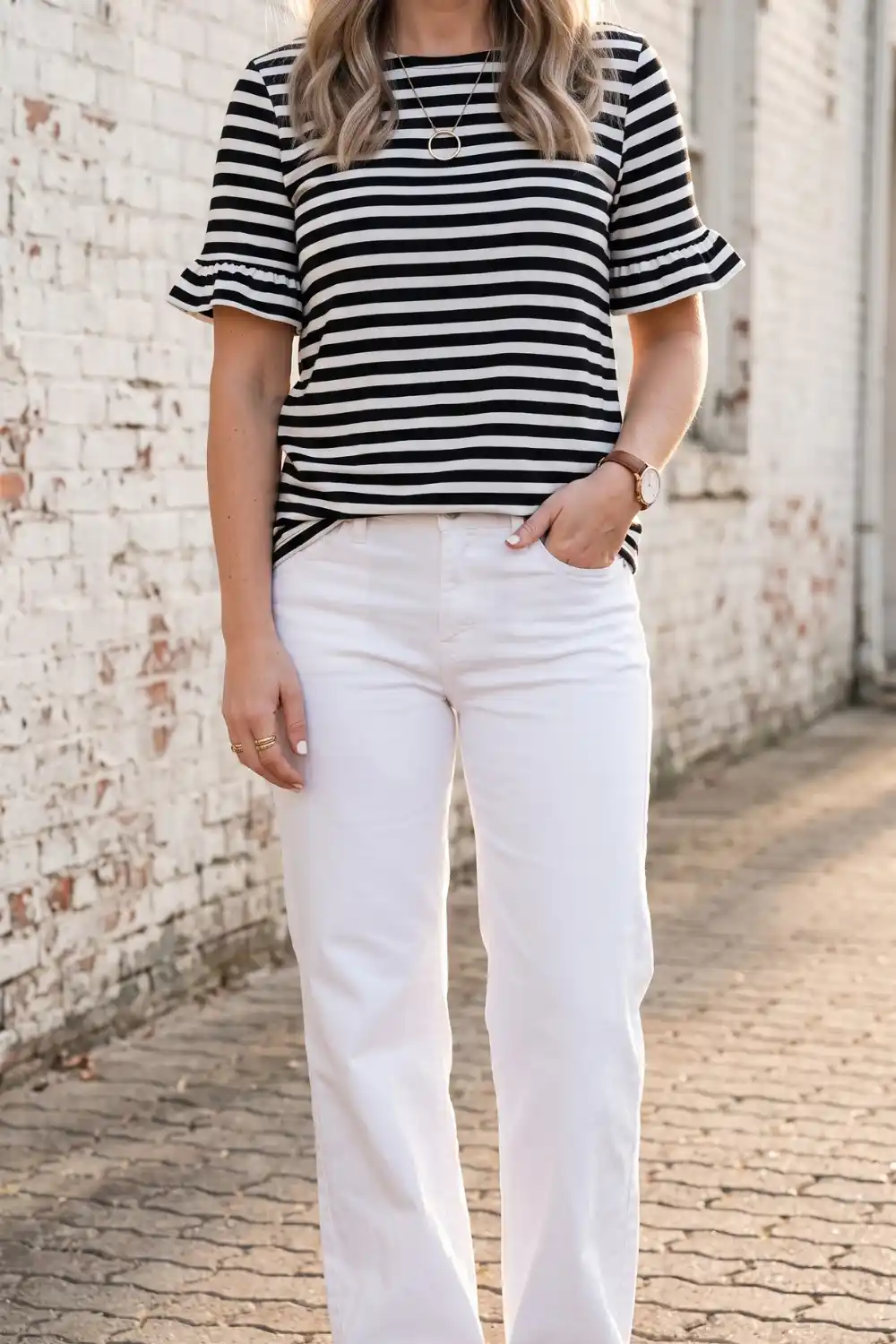 Woman wearing black and white striped ruffle sleeve top with white wide leg jeans