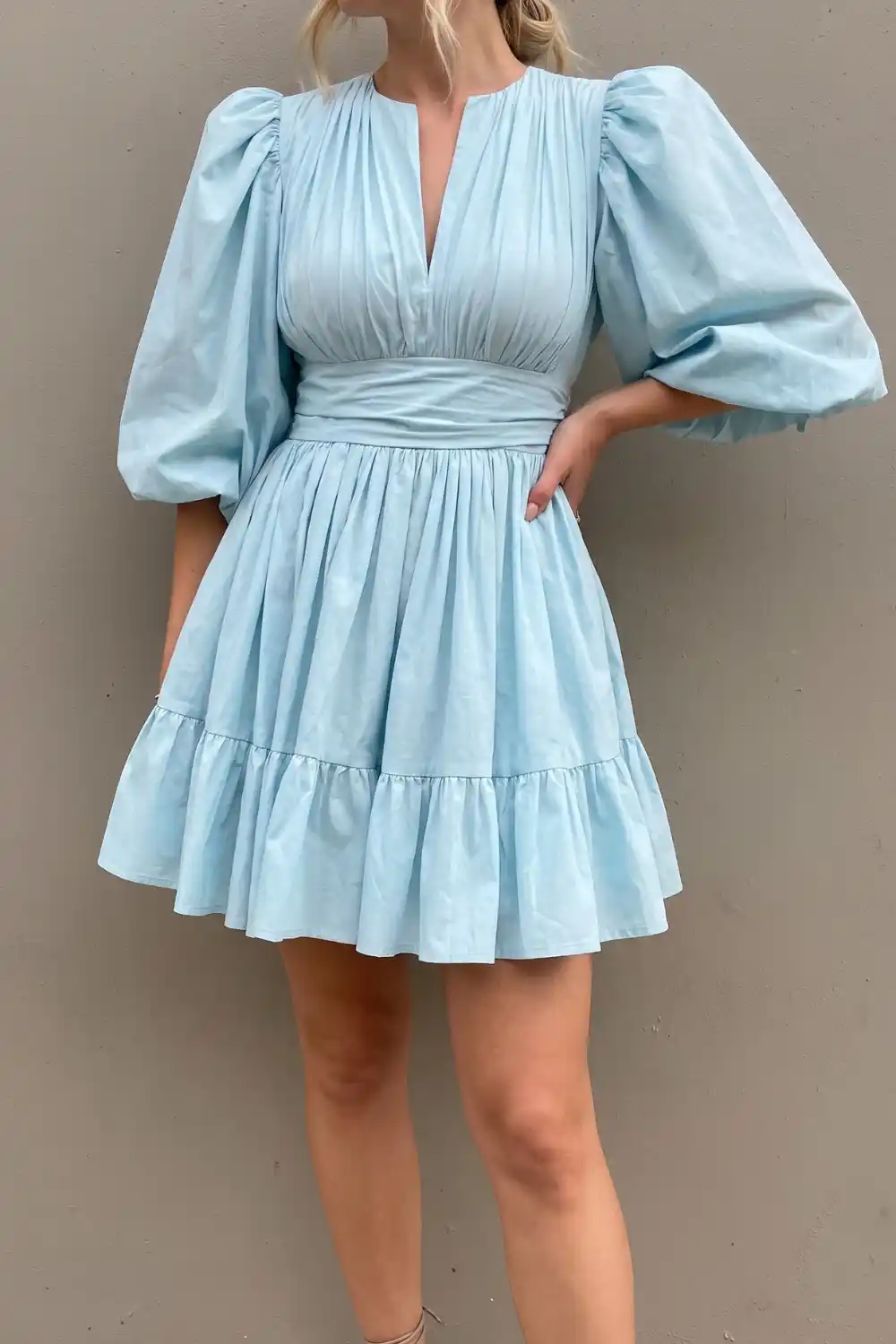Woman wearing light blue puff sleeve tiered mini dress against a grey wall