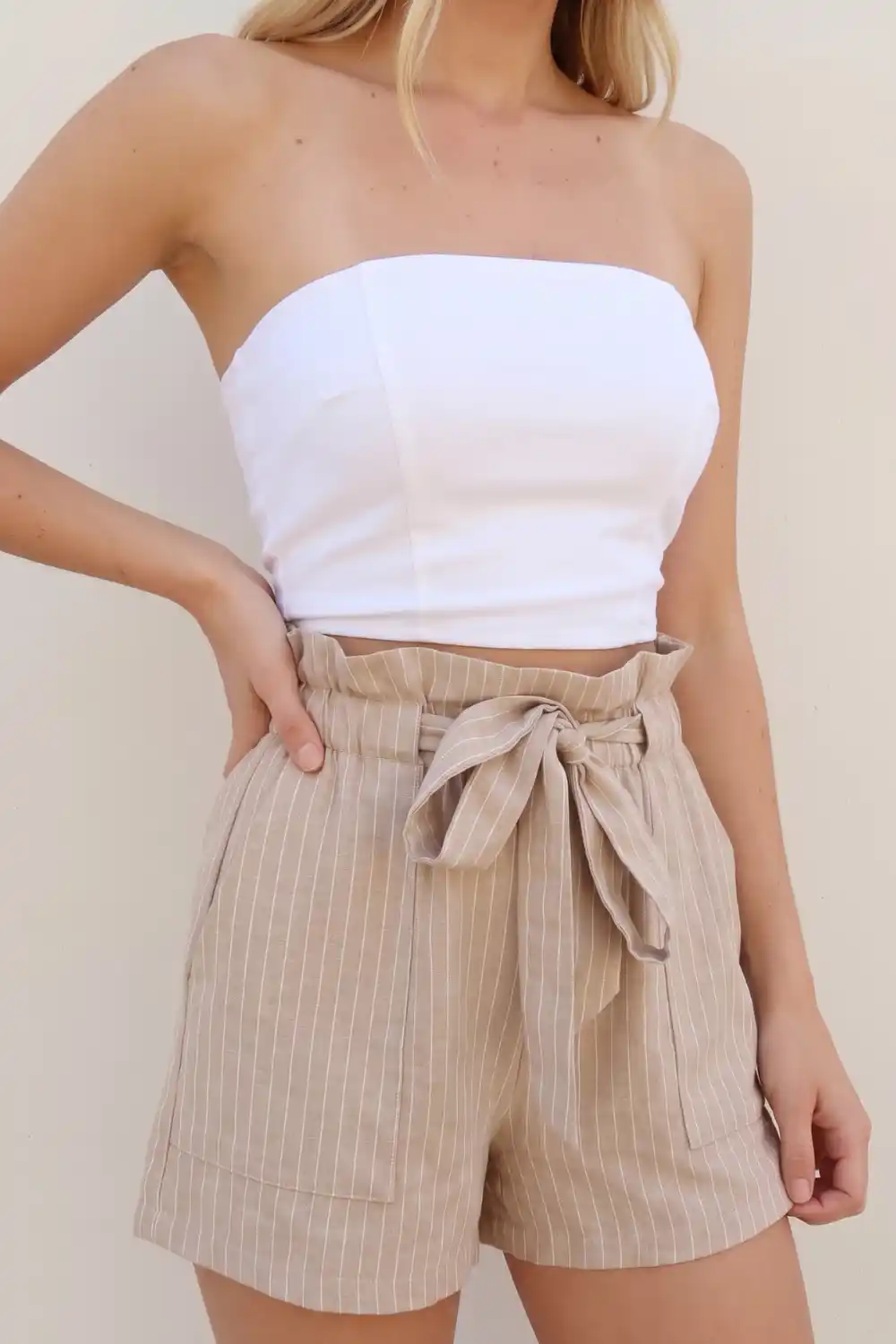 Woman wearing white tube crop top with beige pinstripe paperbag waist linen shorts