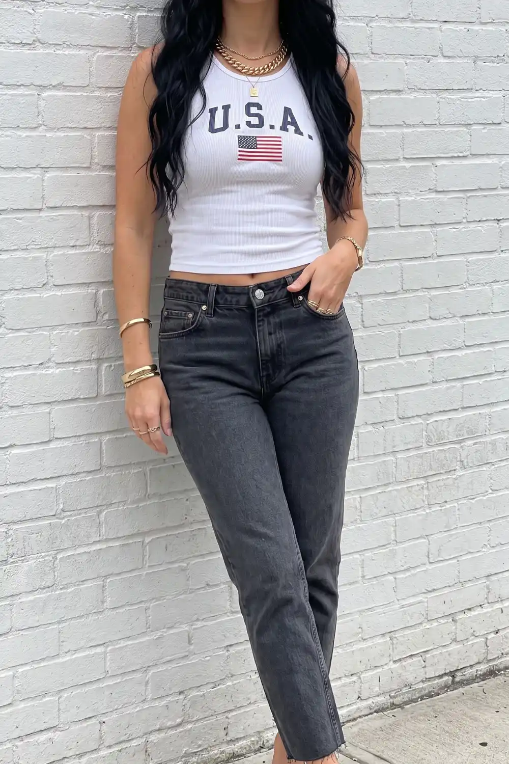 Woman wearing white USA graphic crop tank top with dark grey straight leg jeans