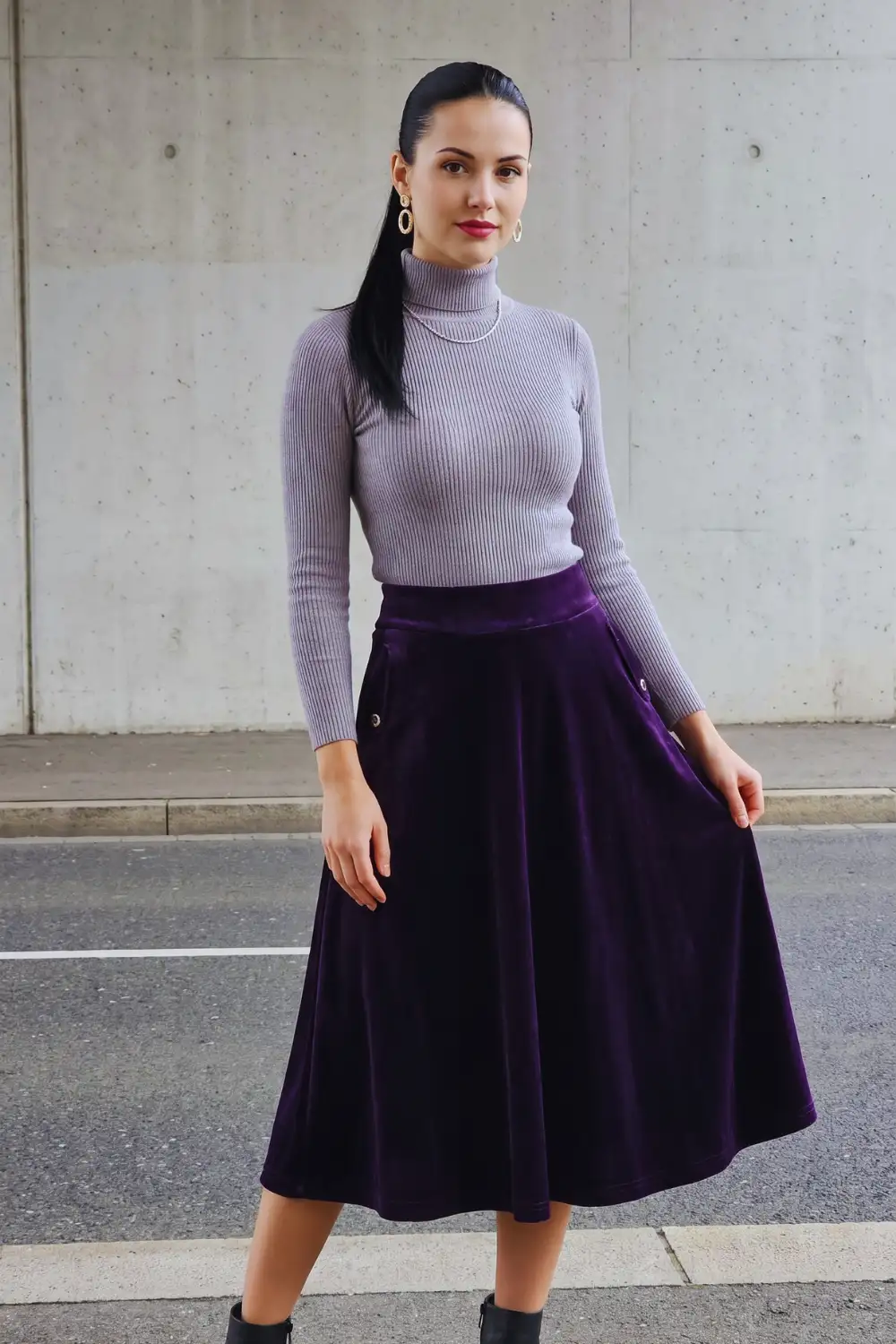 Woman in lavender ribbed turtleneck with deep purple velvet flared midi skirt and black boots