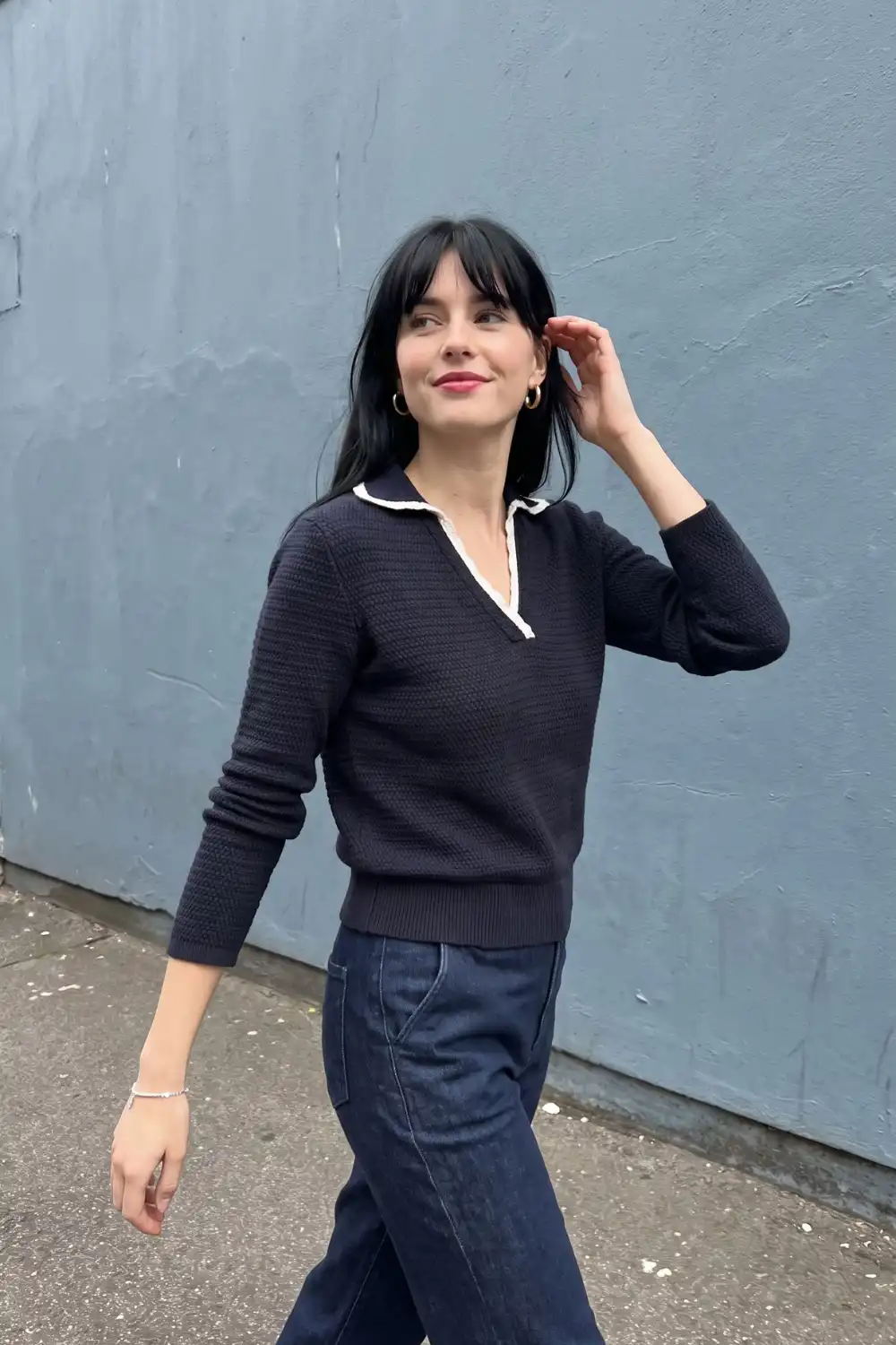 Woman in navy textured polo knit sweater with white collar trim and dark wide leg jeans