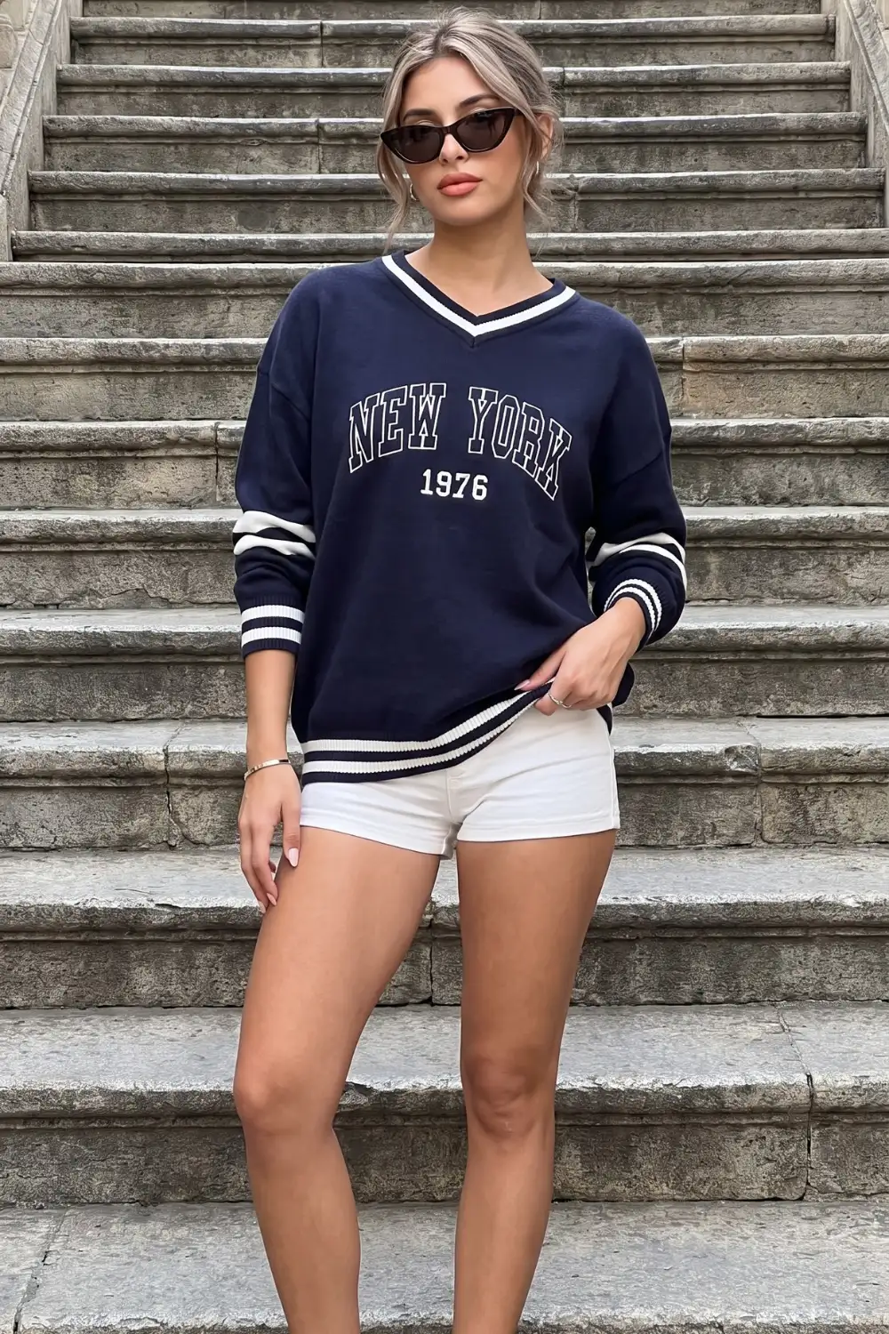Woman in navy blue varsity graphic oversized v neck sweater with white denim mini shorts