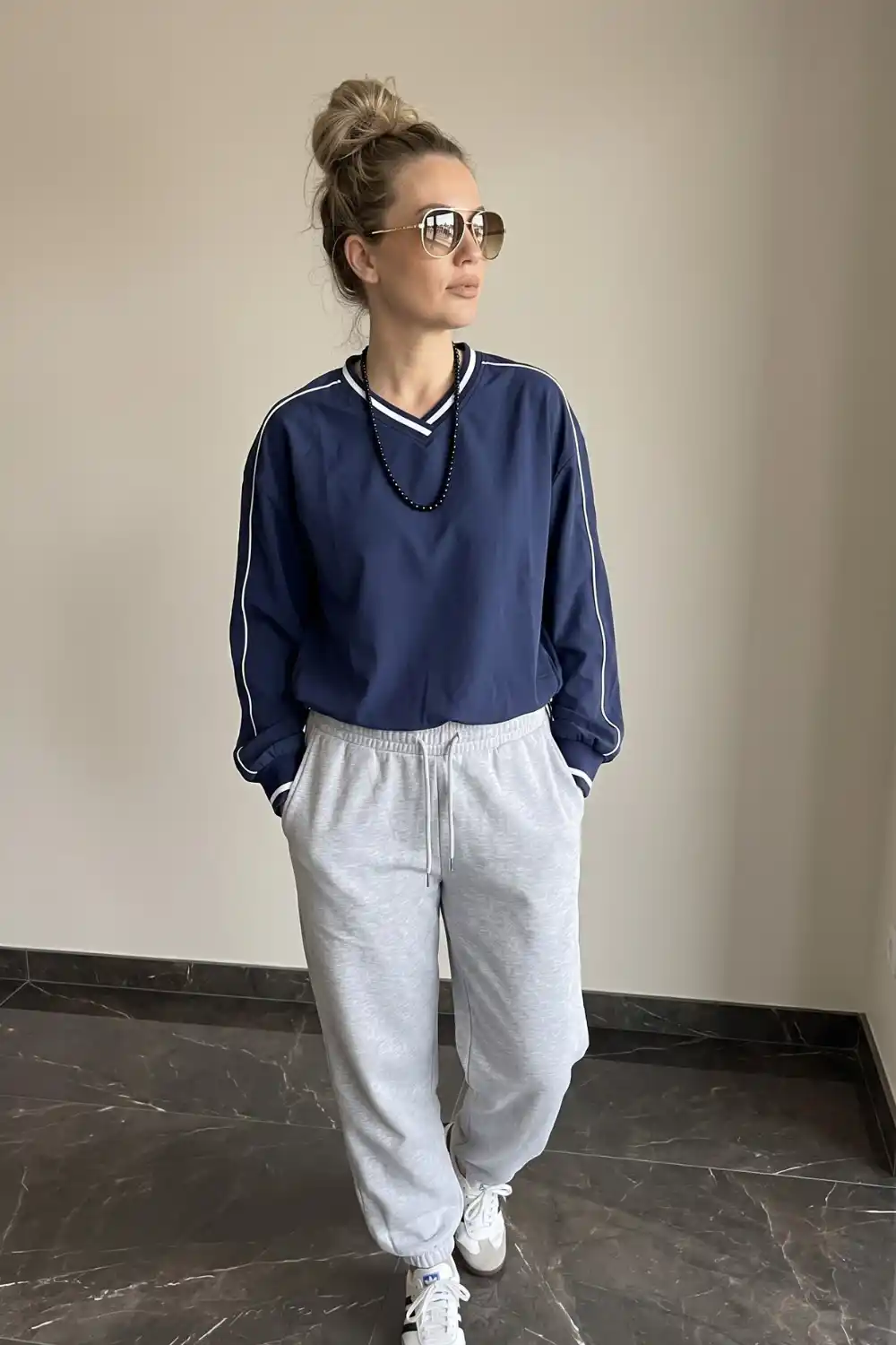 Woman wearing navy blue v-neck sporty sweatshirt with white piping and grey joggers