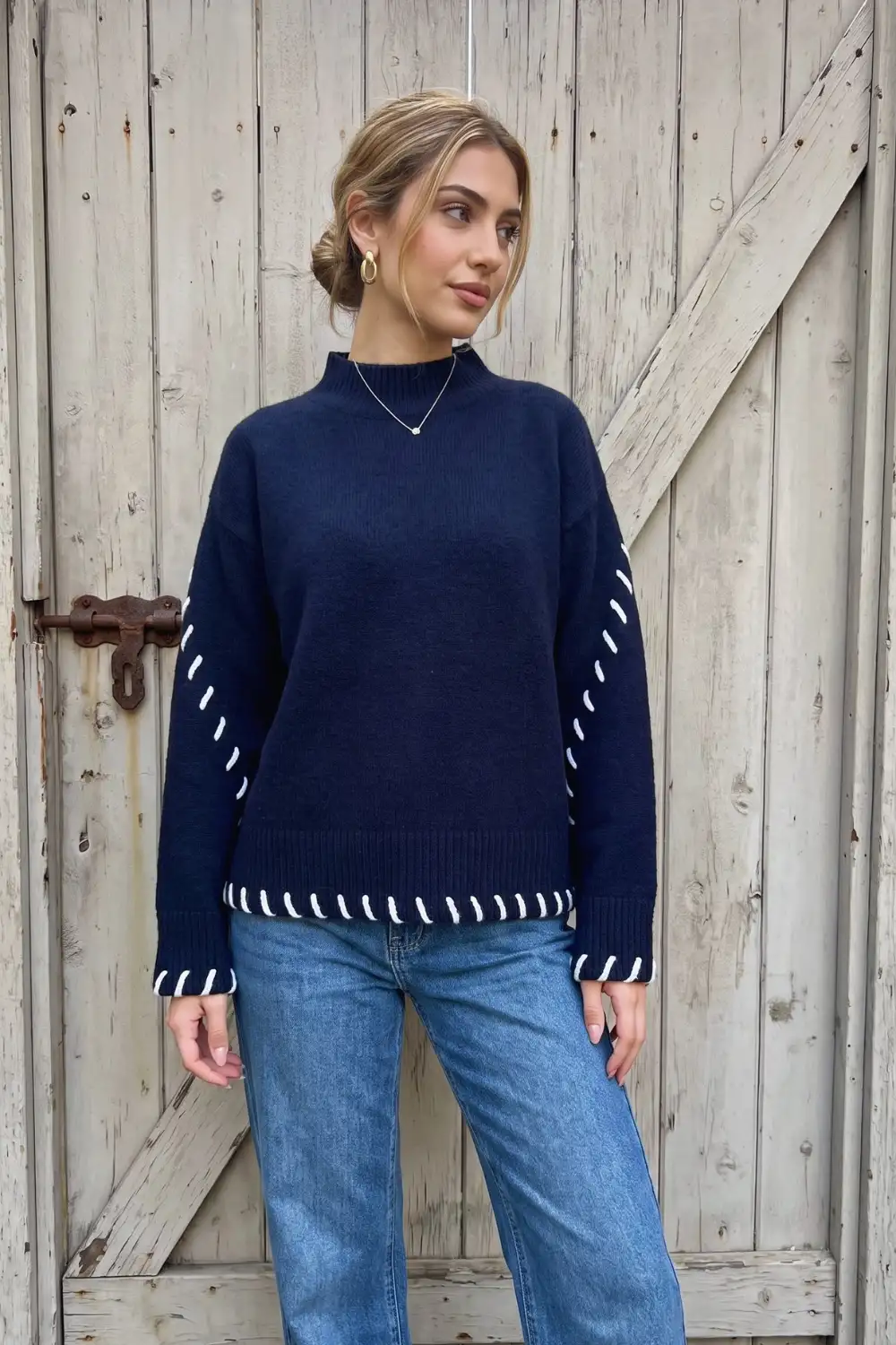 Woman in navy oversized mock neck sweater with white whipstitch trim and mid blue straight leg jeans