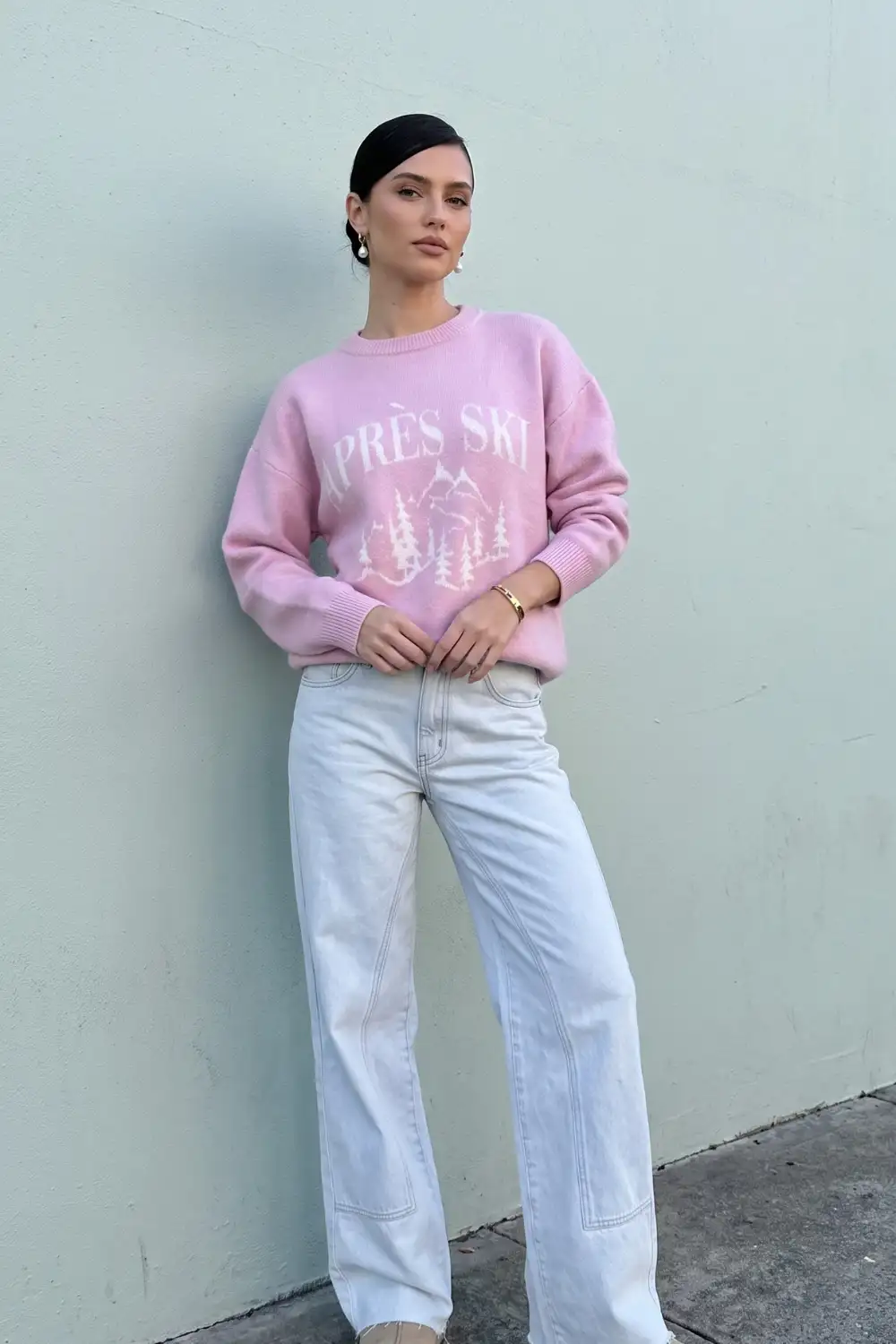 Woman in pink apres ski graphic oversized sweater with light wash wide leg jeans