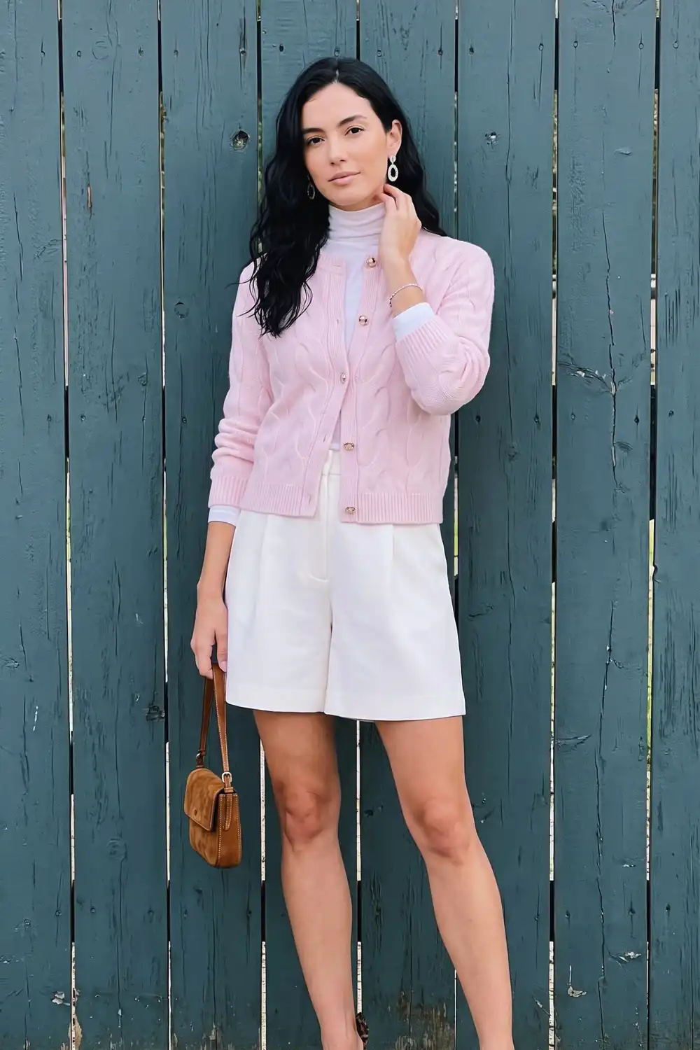 Woman in baby pink cable knit cardigan over white turtleneck with white tailored shorts