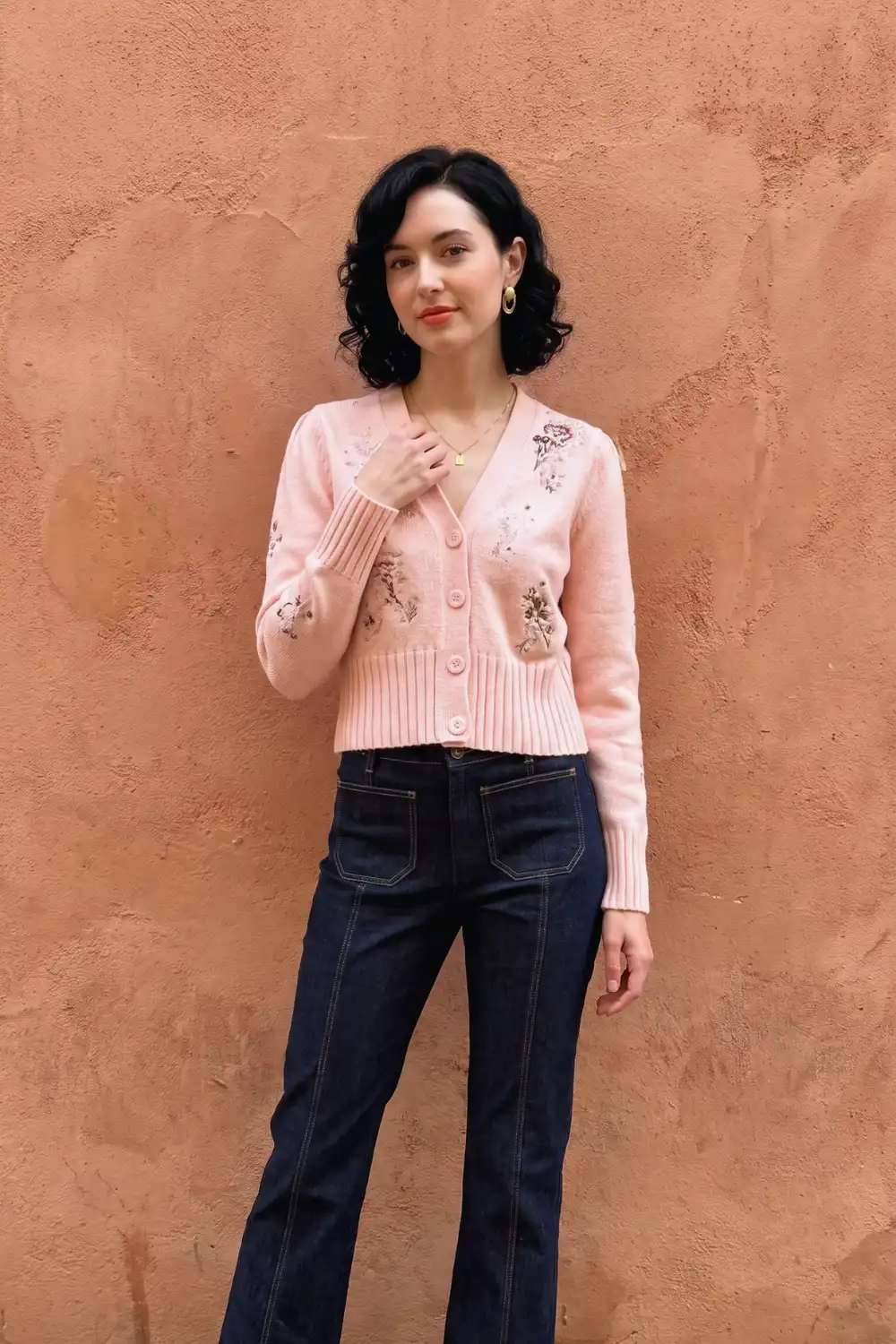 Woman in blush pink floral embroidered cropped cardigan with dark navy flare jeans