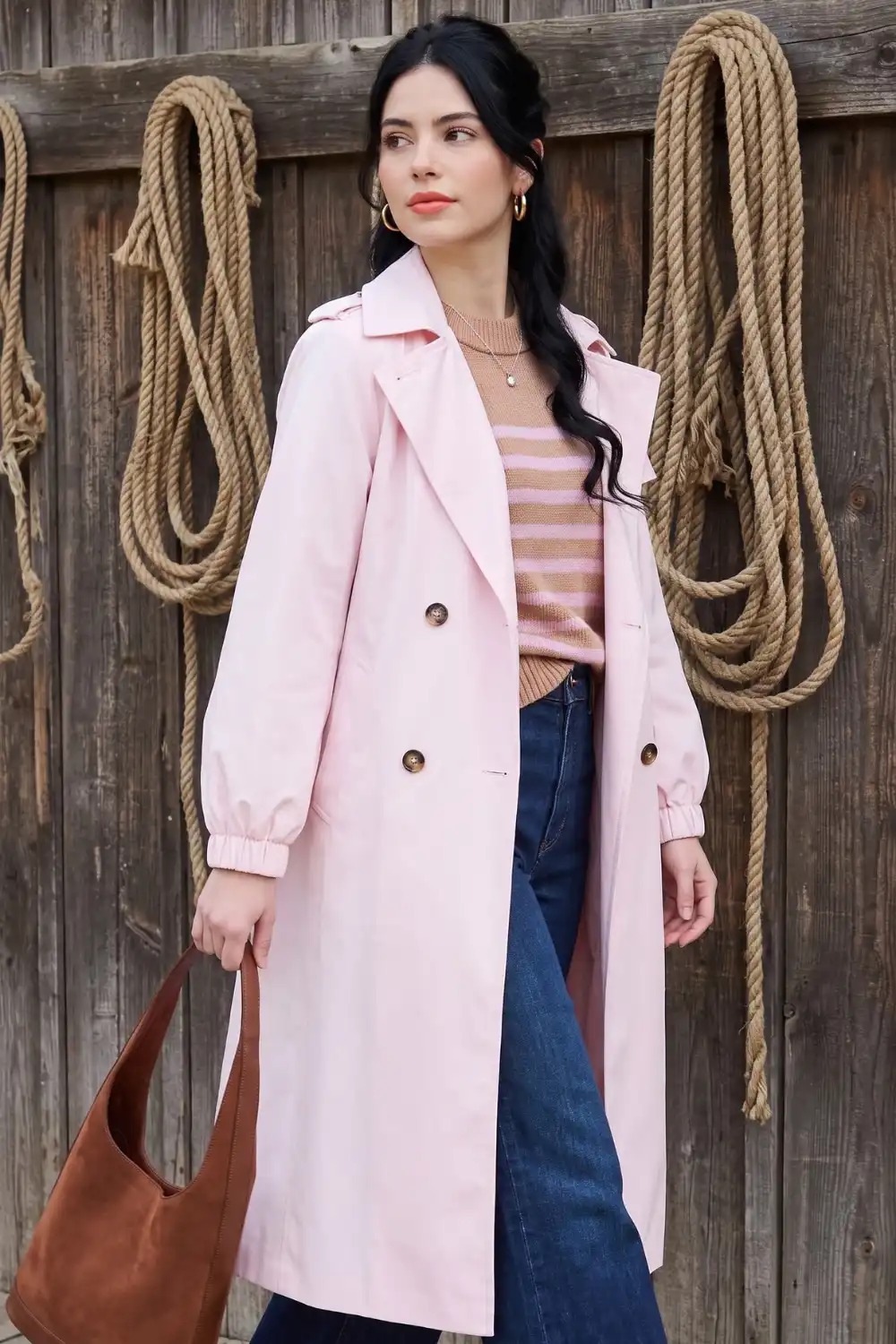 Woman in blush pink trench coat with striped sweater and dark wide leg jeans