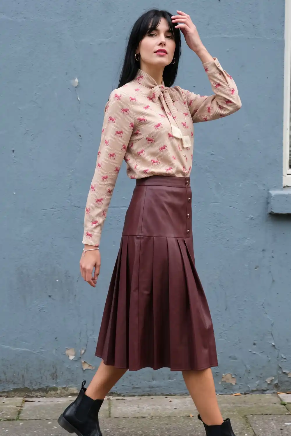 Woman in beige horse print blouse with burgundy pleated leather midi skirt and black ankle boots