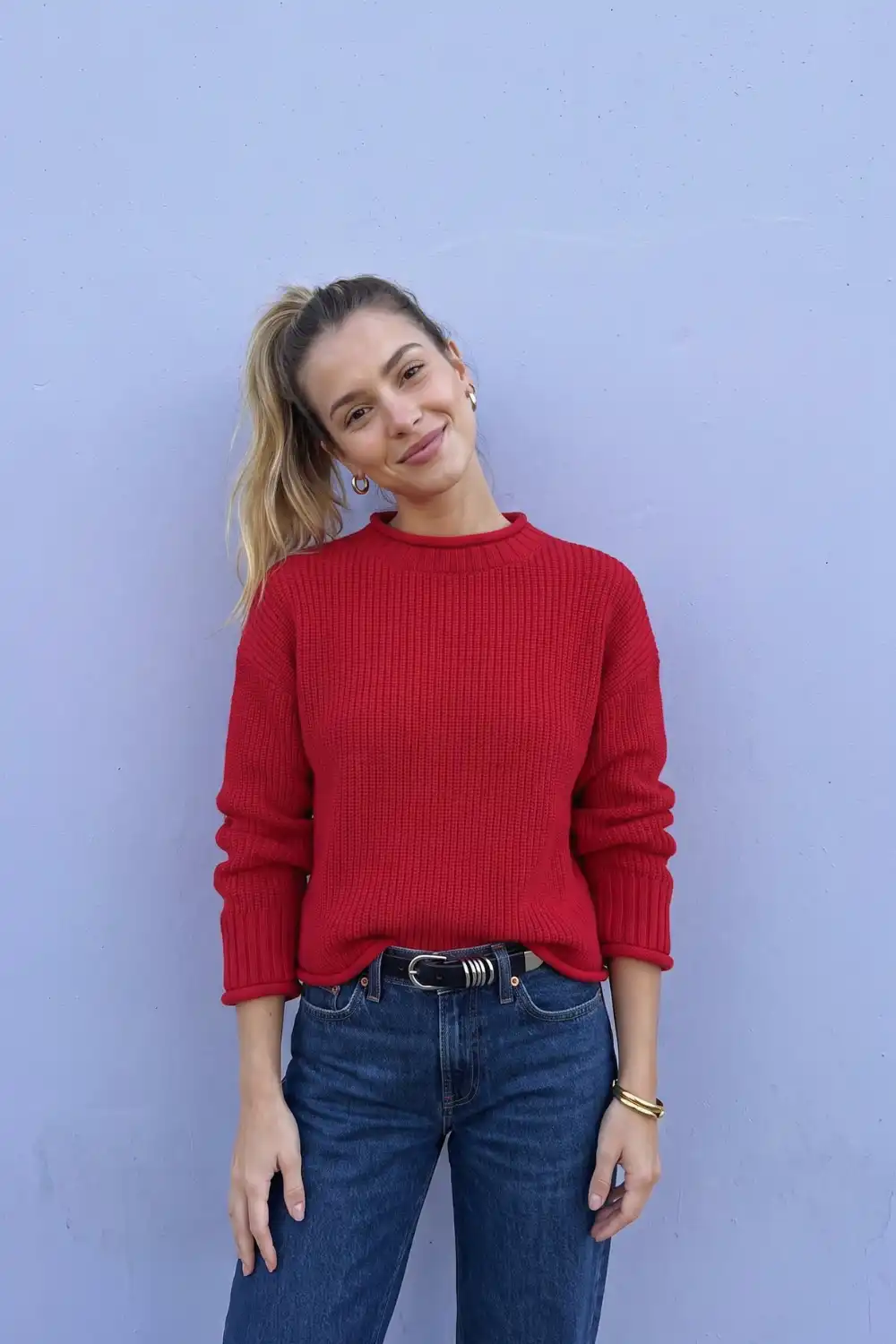 Woman in red chunky ribbed crew neck knit sweater with dark wash straight jeans