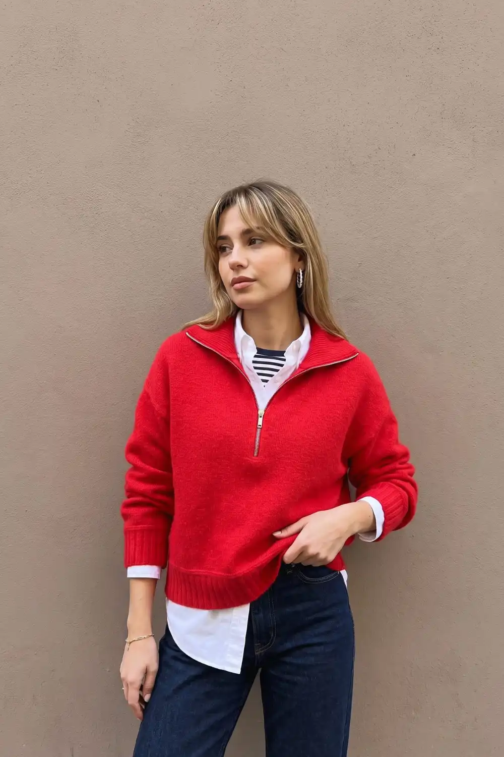 Woman in red half-zip knit sweater layered over white oxford shirt with dark wide leg jeans