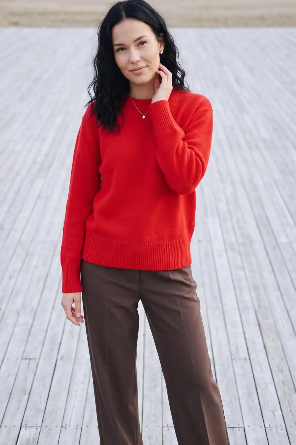 Woman in tomato red relaxed crew neck knit sweater with chocolate brown wide leg trousers