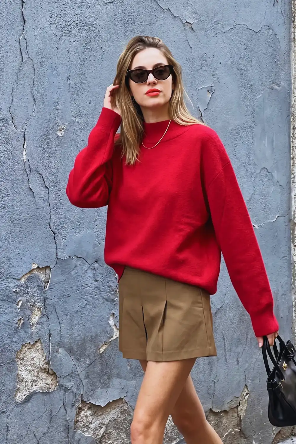 Woman in red oversized mock neck knit sweater with khaki tan pleated mini shorts