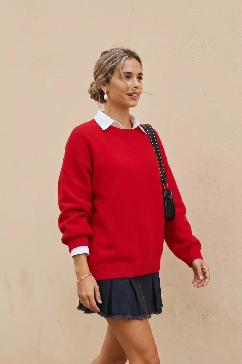 Woman in red oversized crew neck sweater over white collared shirt with dark denim mini pleated skirt